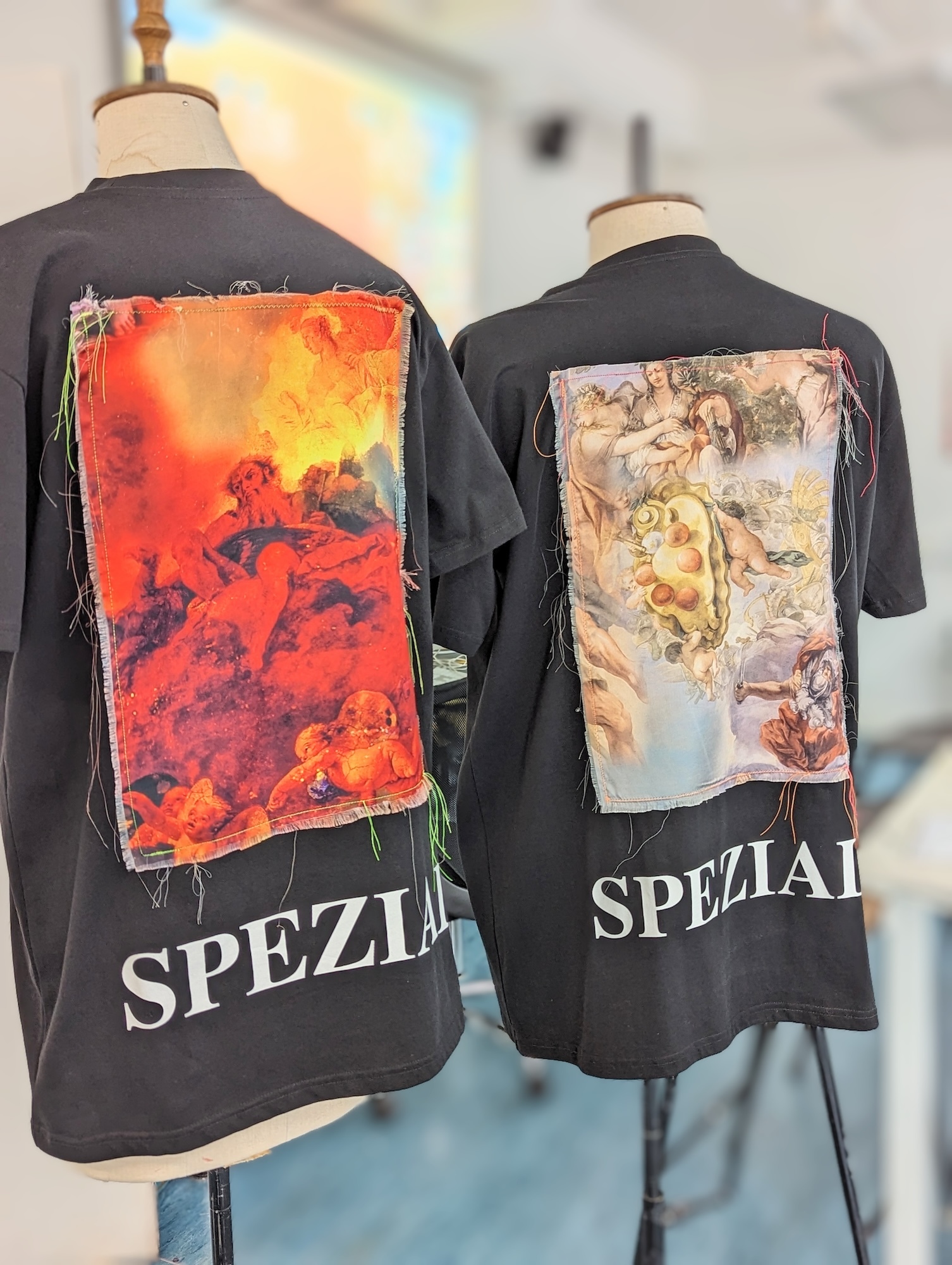 Two T-shirts hanging on mannequins, with classical art-inspired designs loosely sewn onto the backs.