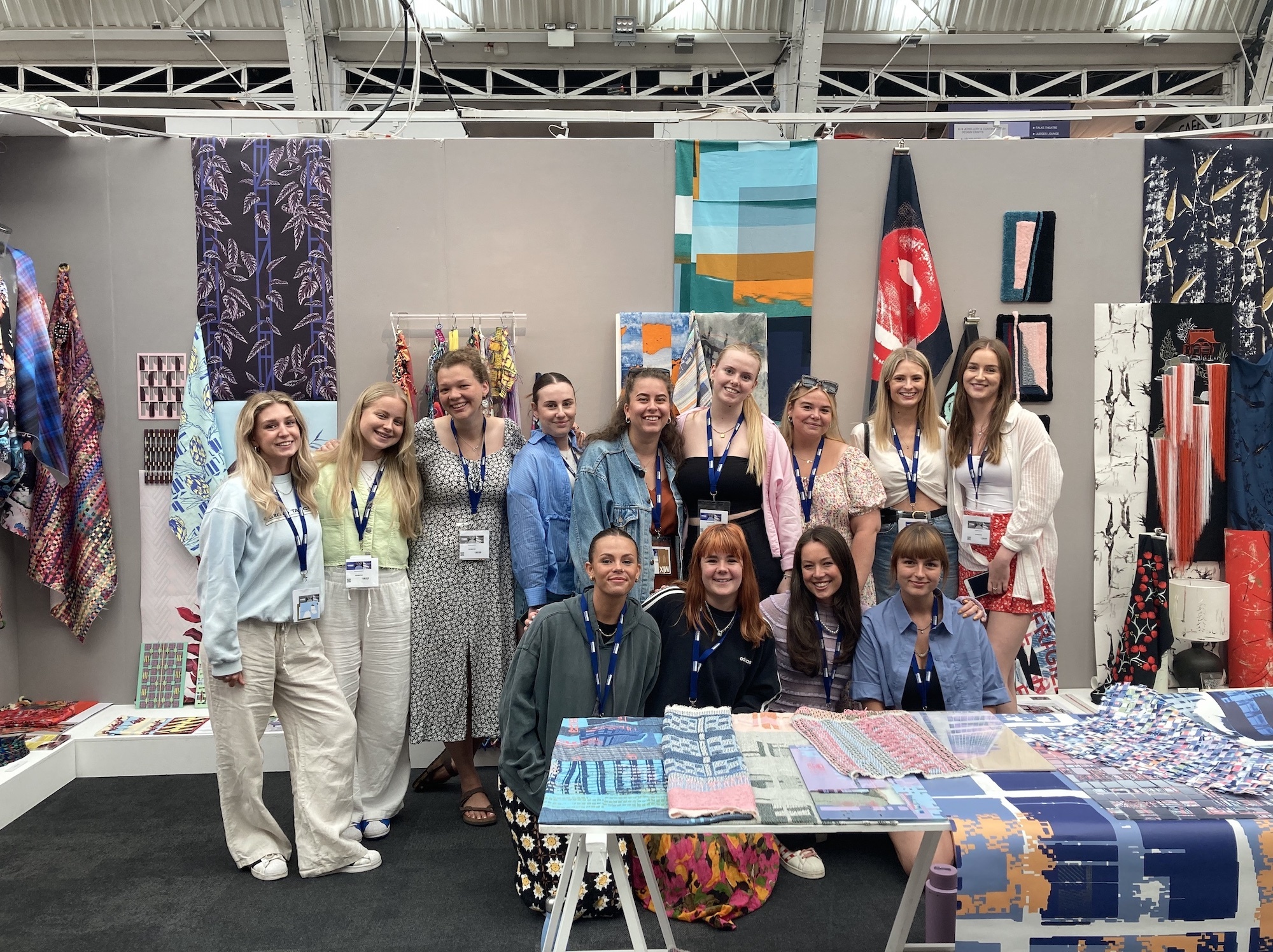 A group of BA (Hons) Textiles students gather and pose for a photo at their stall at the 2023 New Designers show.