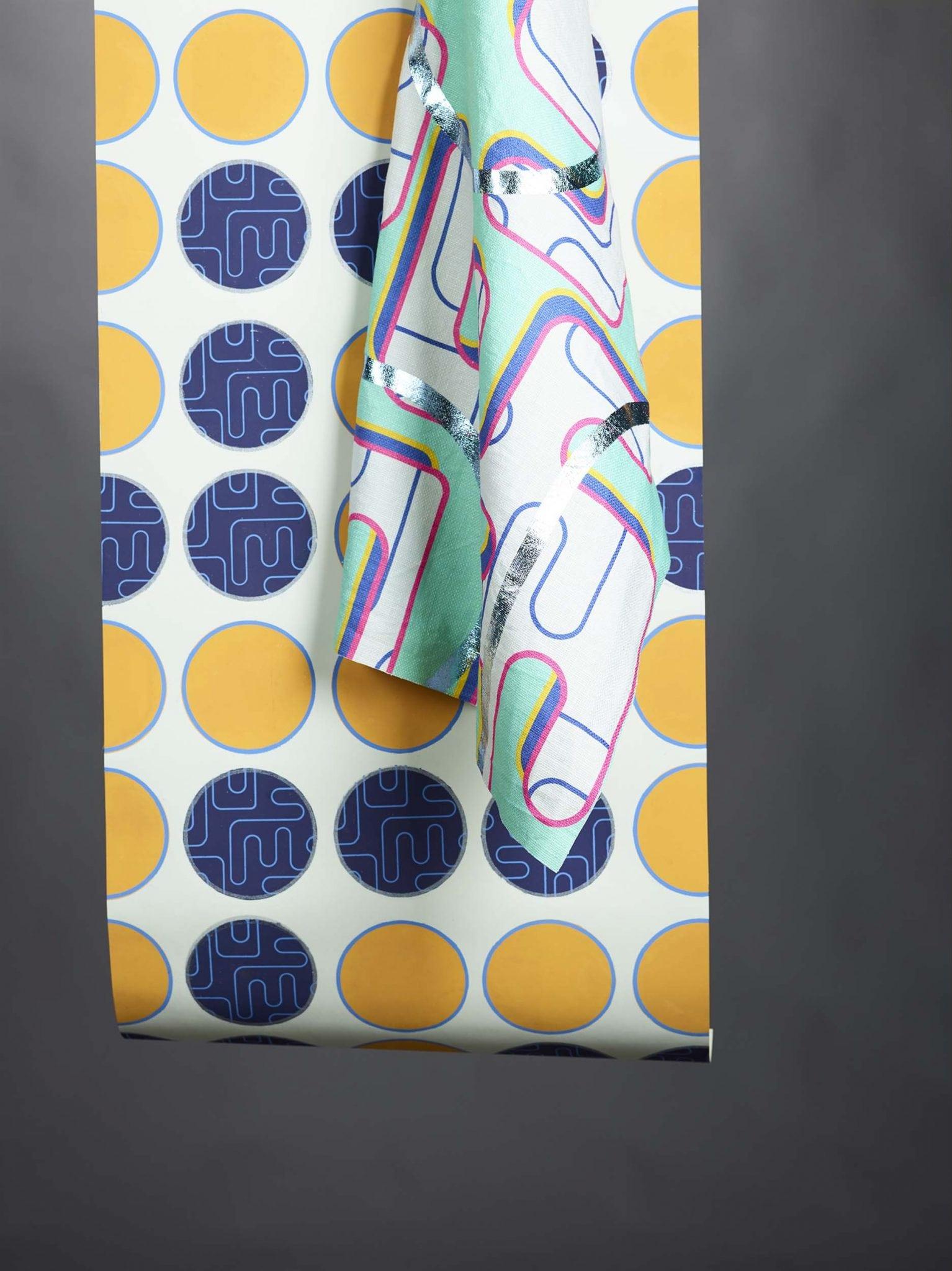 A piece of fabric hangs against a roll of paper with a circle pattern.
