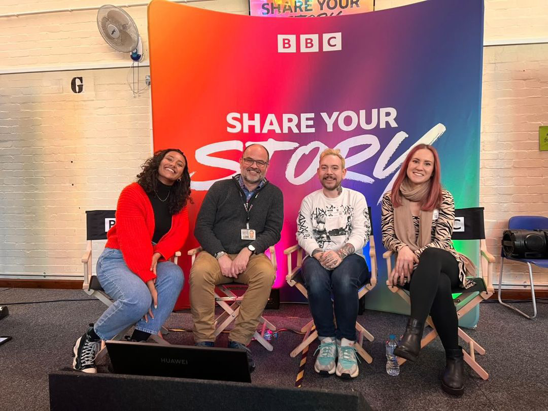 Four people sitting in seats in a BBC studio, with a colourful backdrop behind them. Text reading "Share your story" appears on the backdrop.