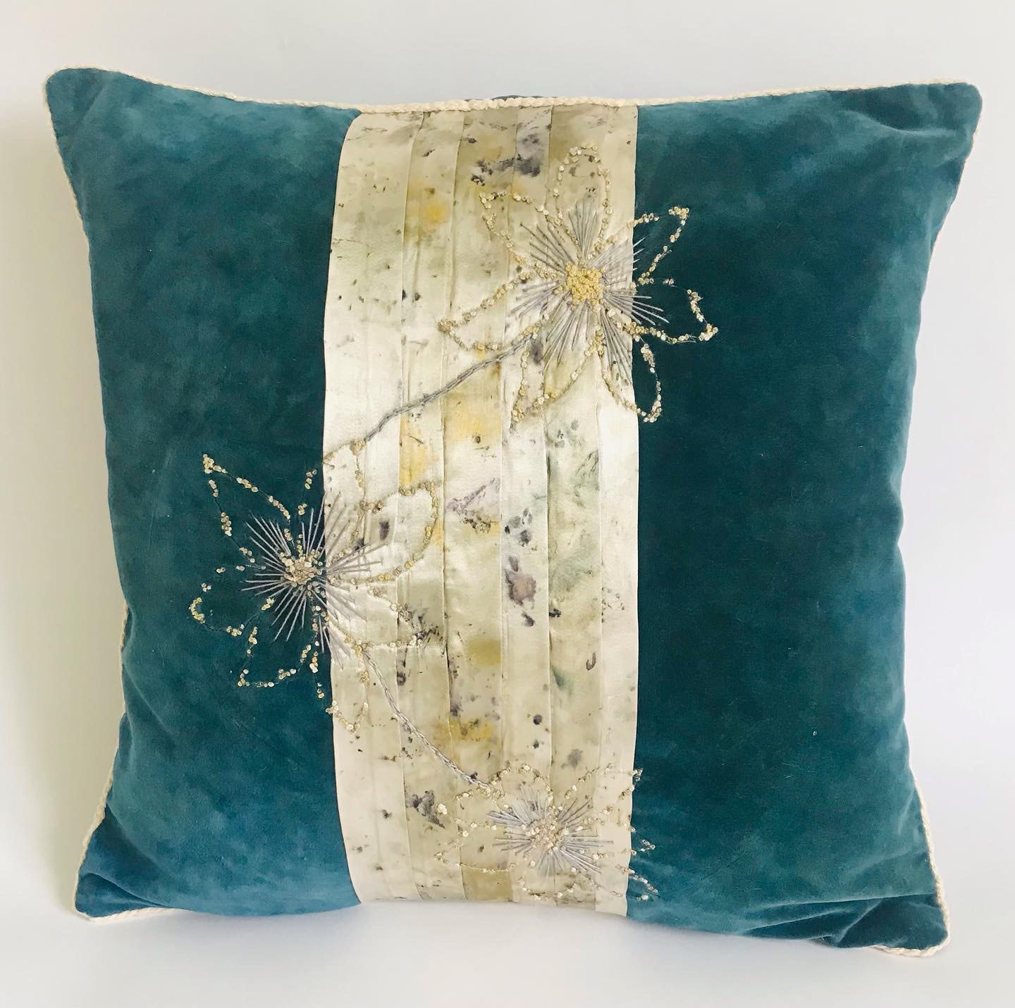 Teal velvet cushion with central cream panel featuring gold embroidered dandelion seed heads and scattered sequins or beads.