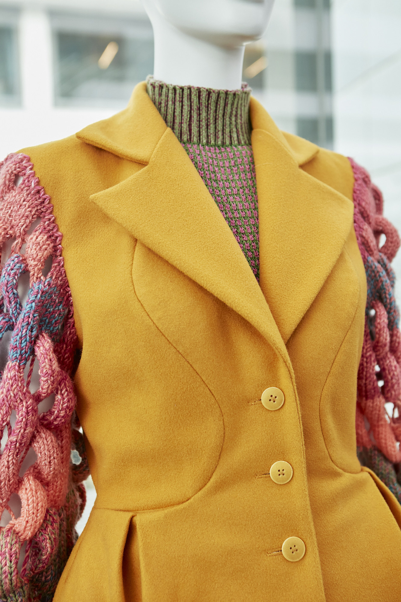 Yellow coat with buttons and red fabric-woven arms on mannequin.