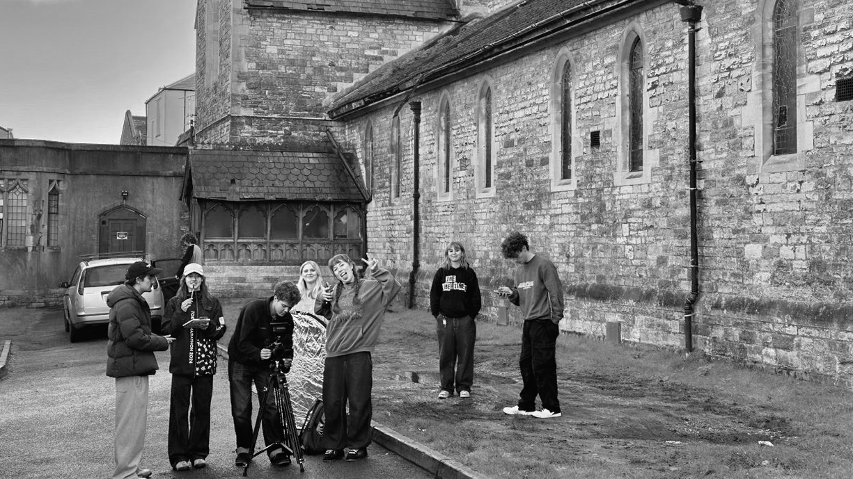 Black and white image of people gathered outside stone church building with arched windows and medieval architecture.