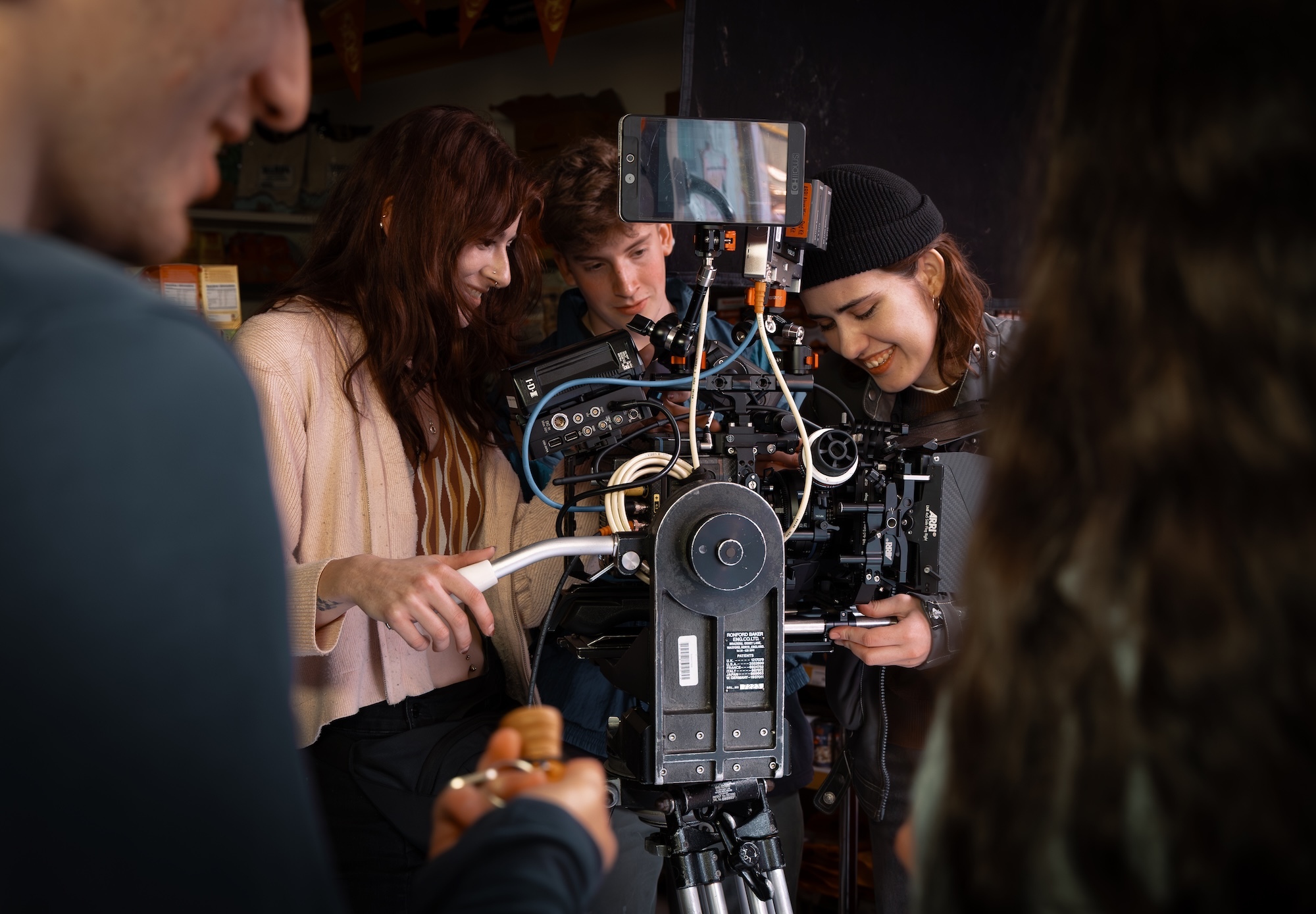 Crew of BA (Hons) Film Production students operating professional camera equipment, with three people gathered around black camera rig and monitor in dark setting.