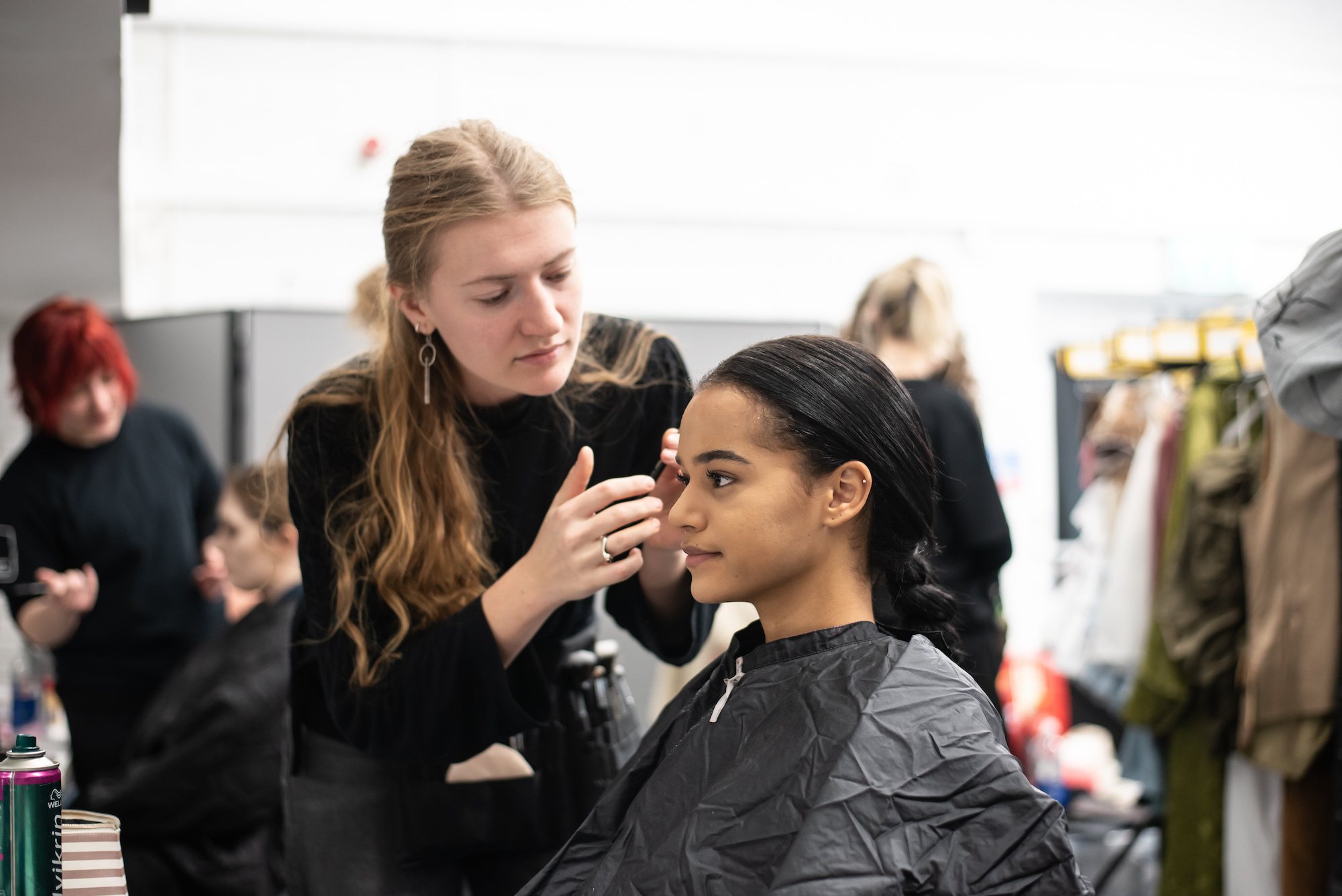 A BA (Hons) Make-up for Media and Performance student applies make-up to a BA (Hons) Acting student who is sitting in a make-up chair.