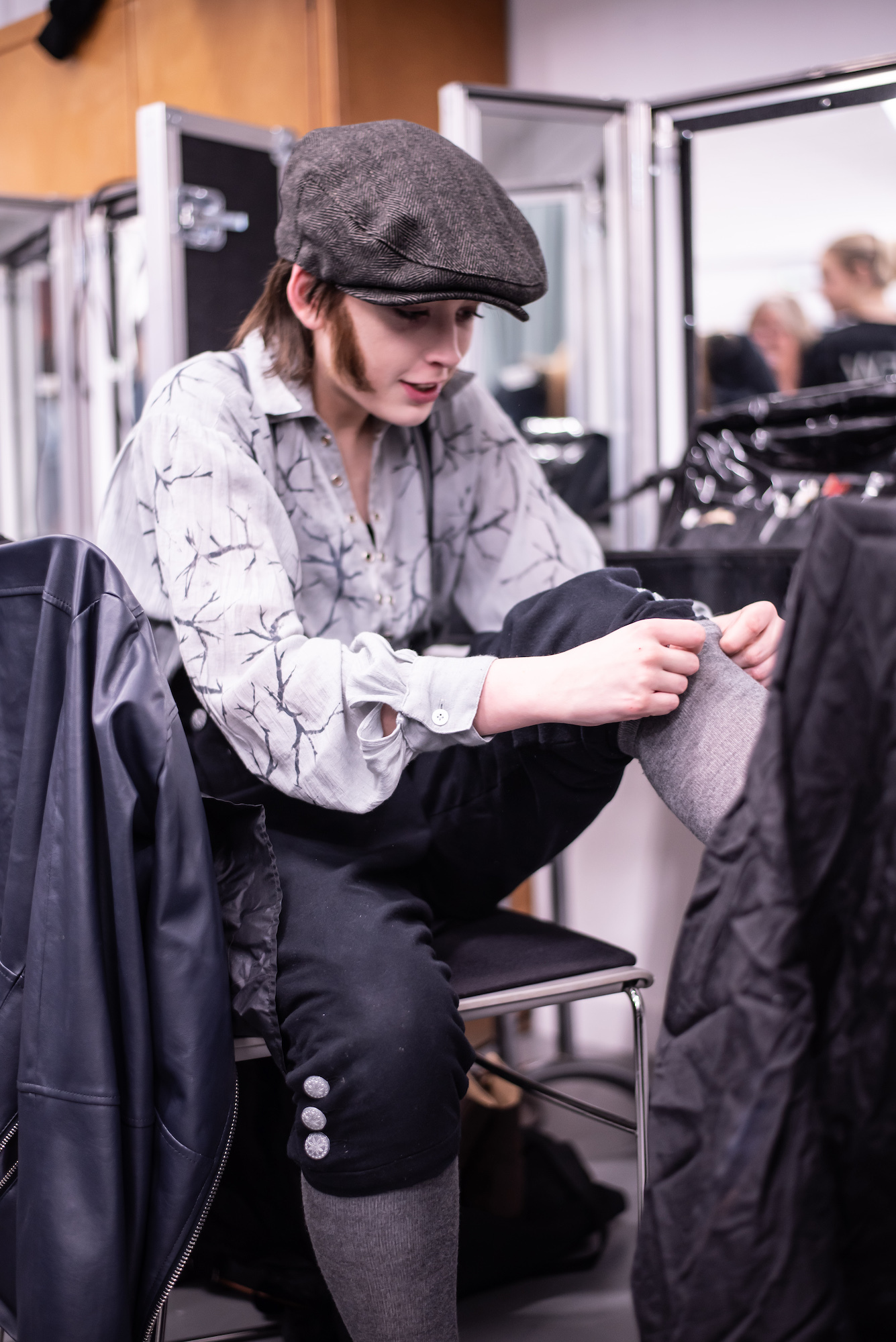 A BA (Hons) Acting student sitting backstage adjusting one of their stockings, behind the scenes on "The Wolves of Willoughby Chase".
