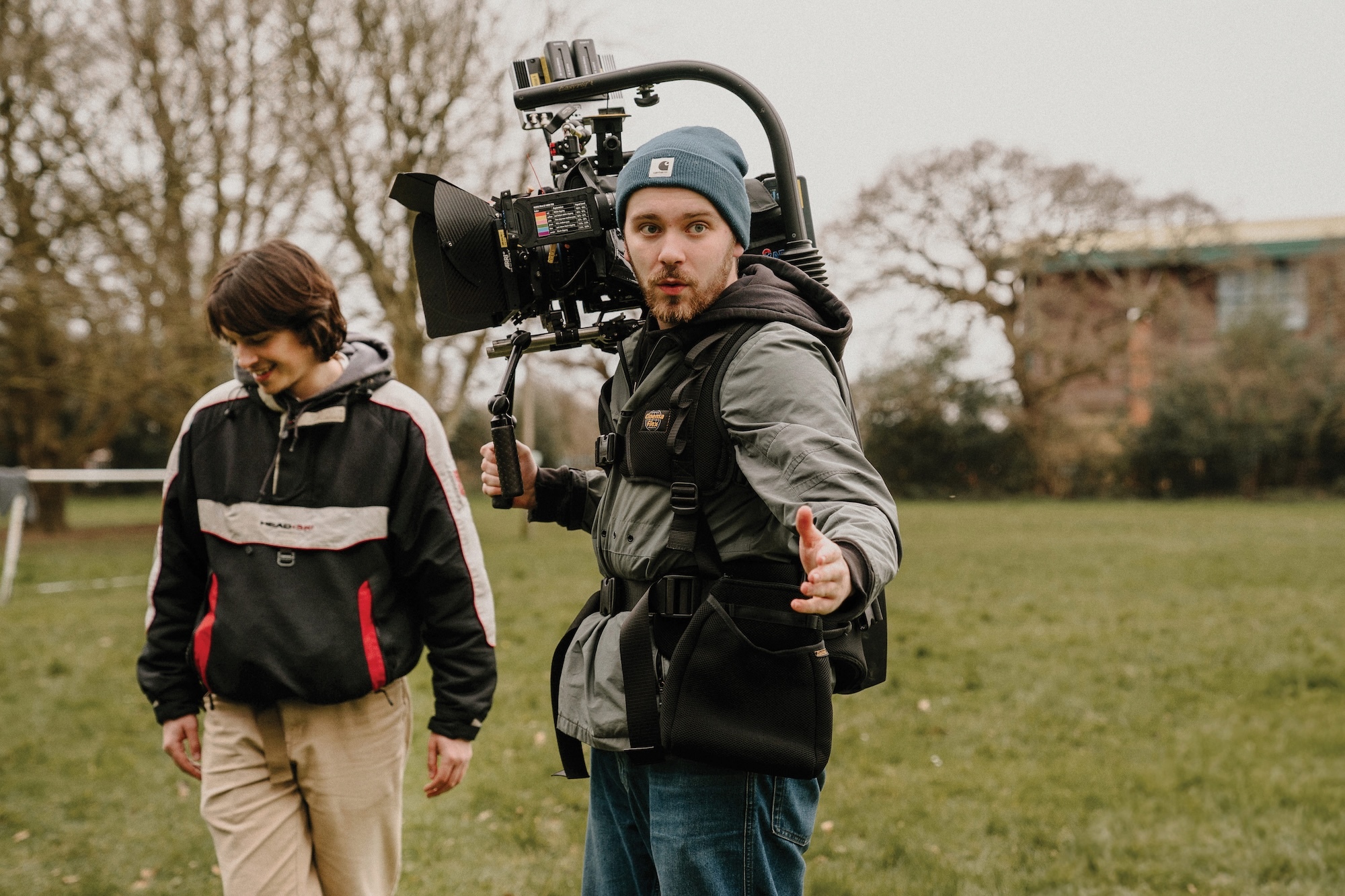Two BA (Hons) Film Production students filming outdoors with professional camera equipment, one operating steadicam rig, bare trees and buildings in background.