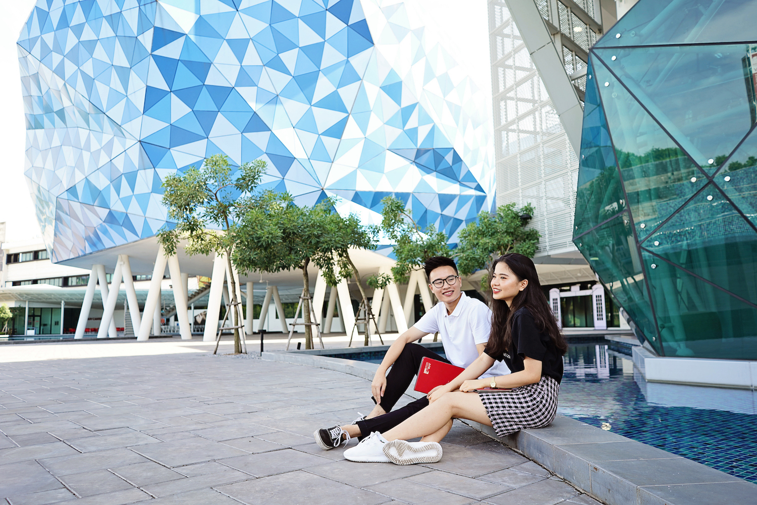 Two students sitting outside abstract buildings on campus at British University Vietnam (BUV)