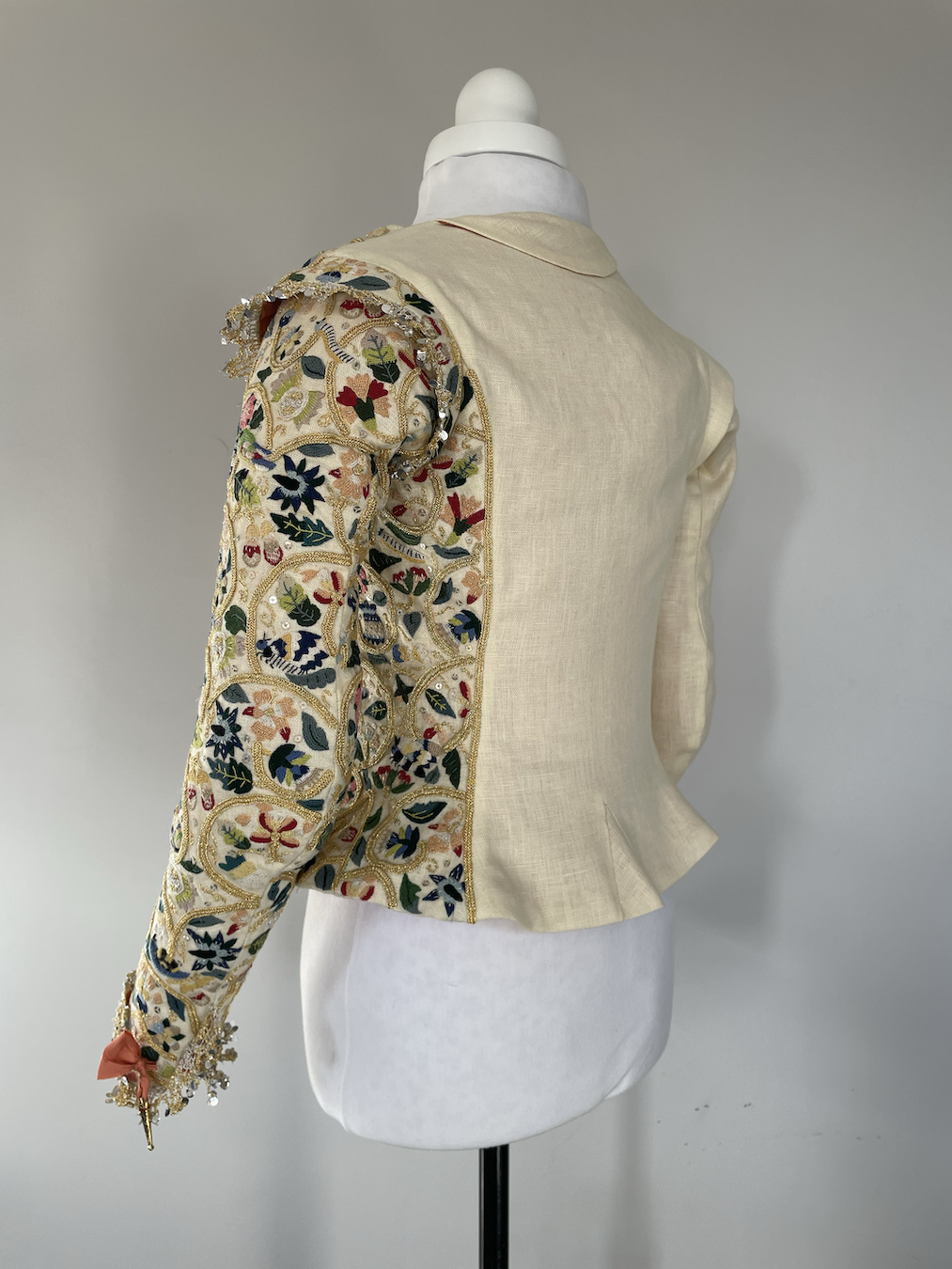 A 1610s jacket with ornate embroidery on one side, displayed on a mannequin and viewed from the back.