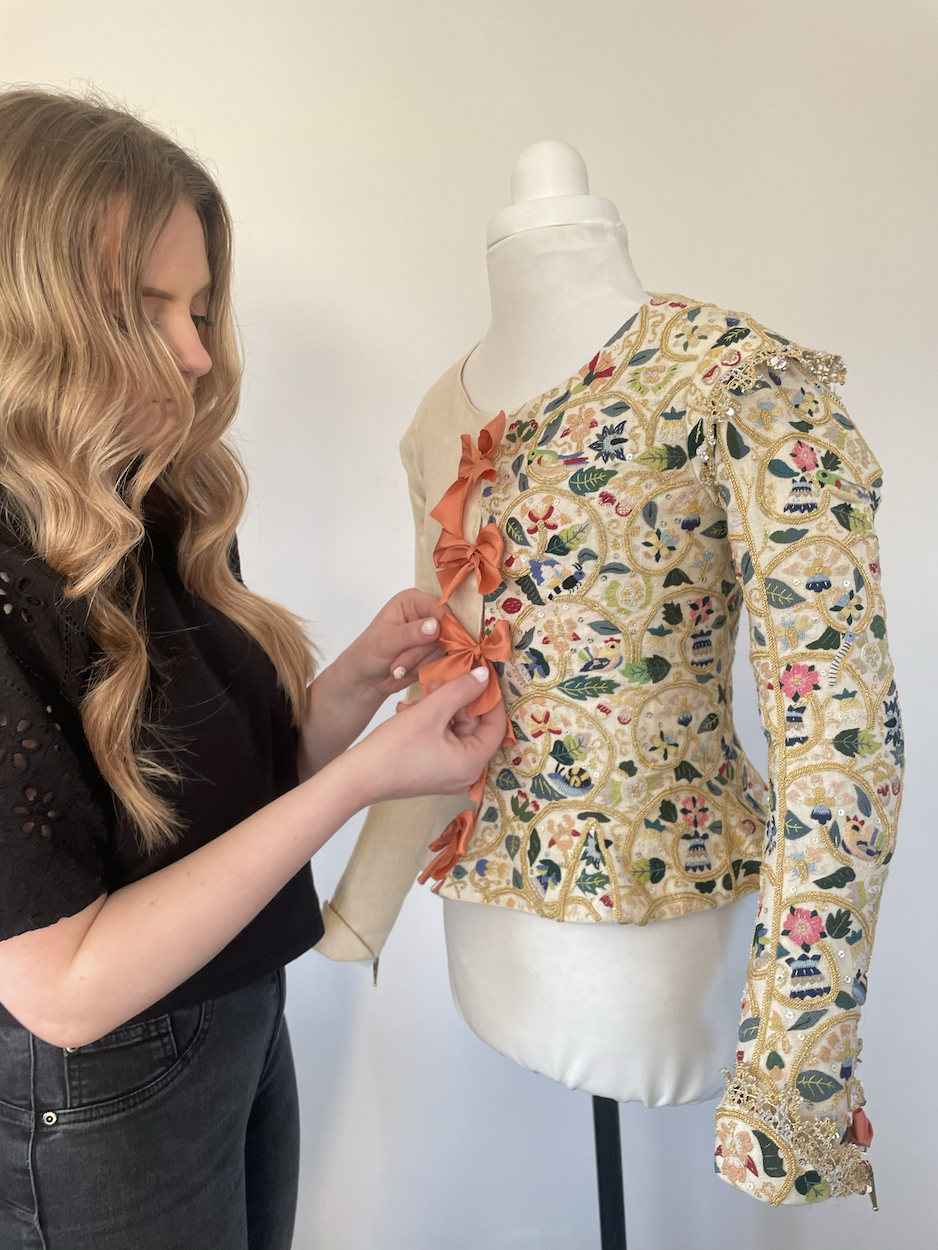 BA (Hons) Costume student tying a ribbon on the front of a 1610s jacket on a mannequin.