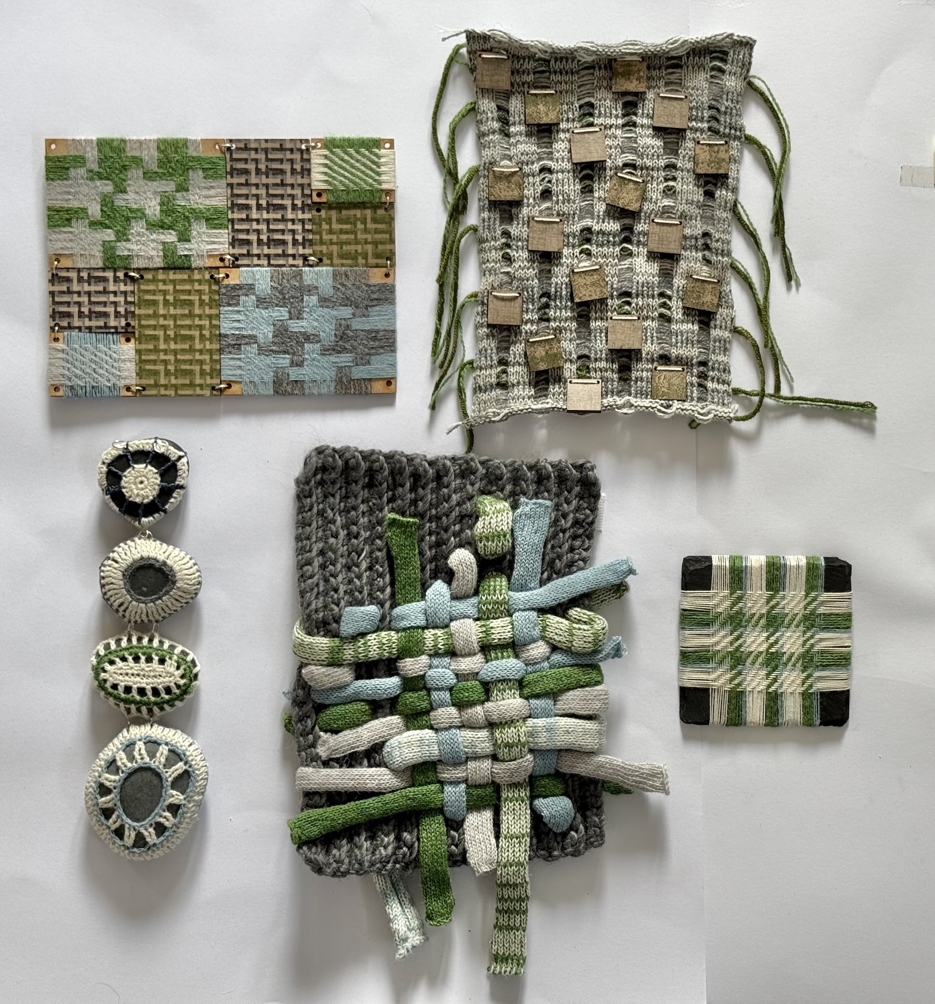Textile art samples in green, brown, and grey tones featuring woven patterns, frayed edges, and layered fabric strips arranged on white wall.
