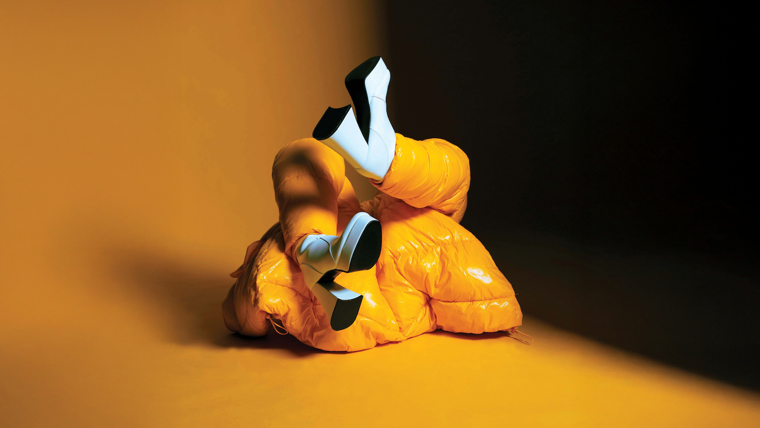 Orange and yellow plush toy dog lying on wooden surface with warm lighting and dark background.