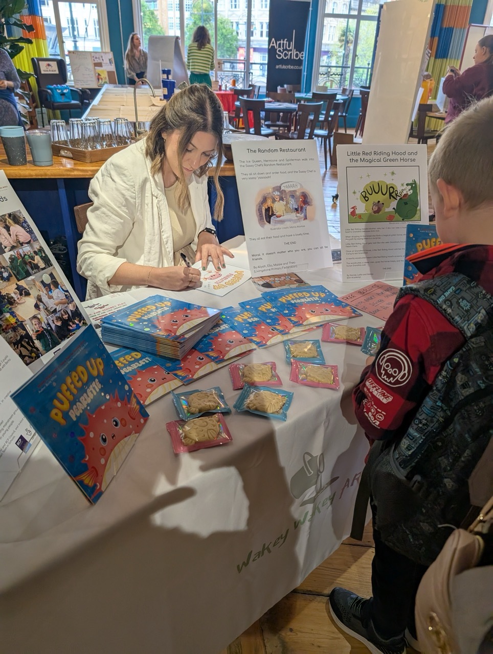 Becky White signing copies of Puffed Up Pearlette and talking to a boy by the stand.