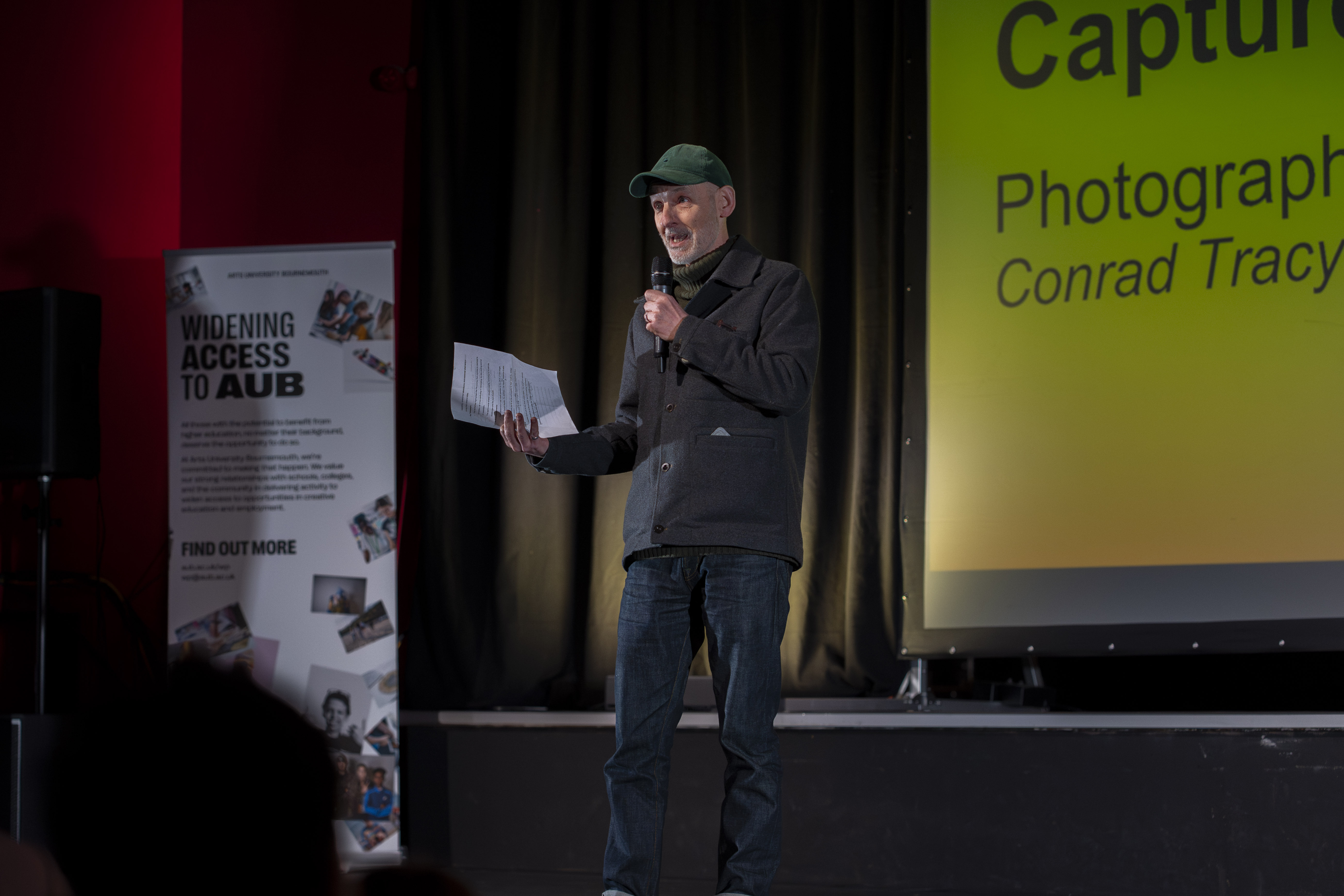 A member of staff speaking on stage about the workshop they delivered with the workshop title displayed behind them