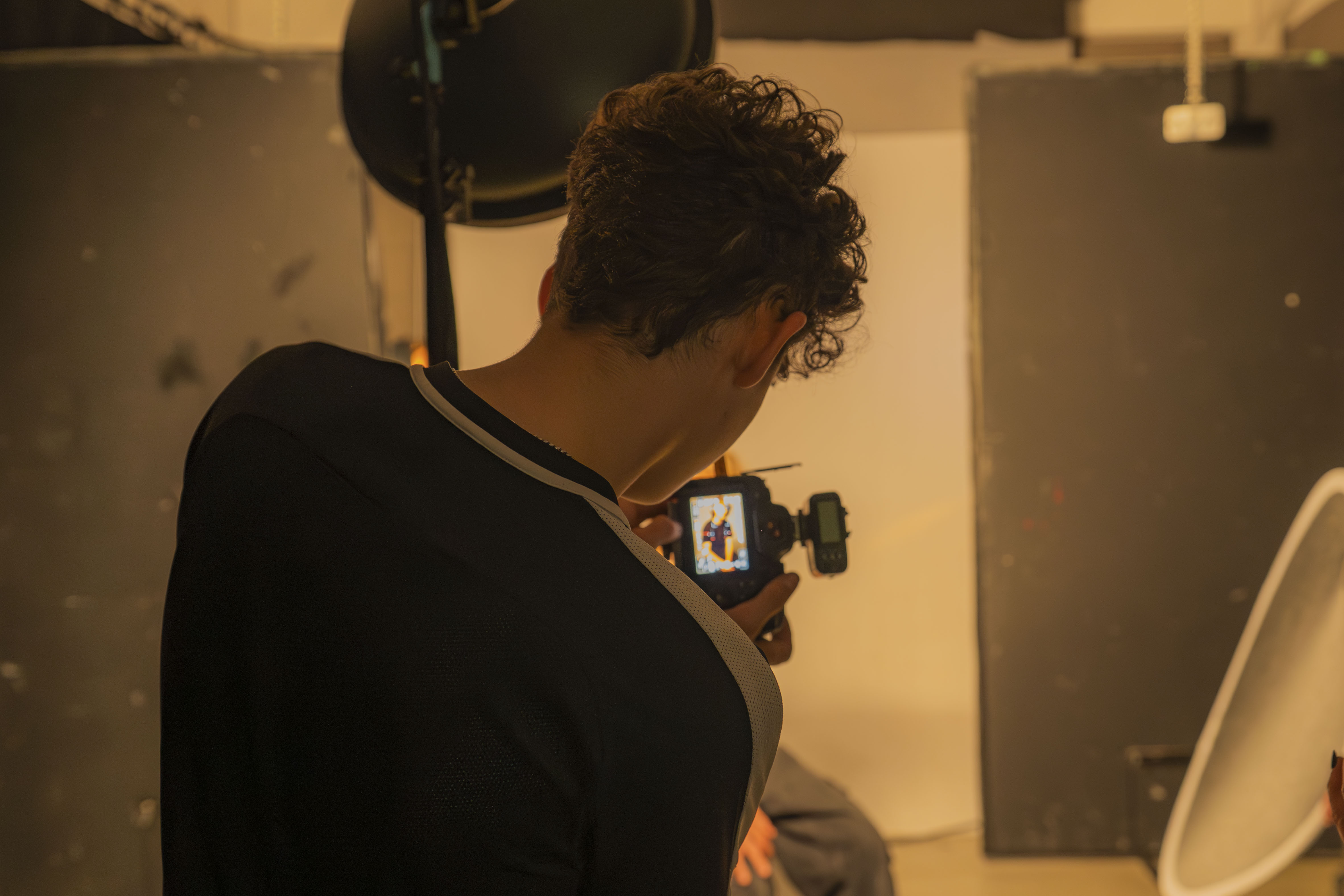 Boy holding a camera in portrait, screen and orange light blurred in background.