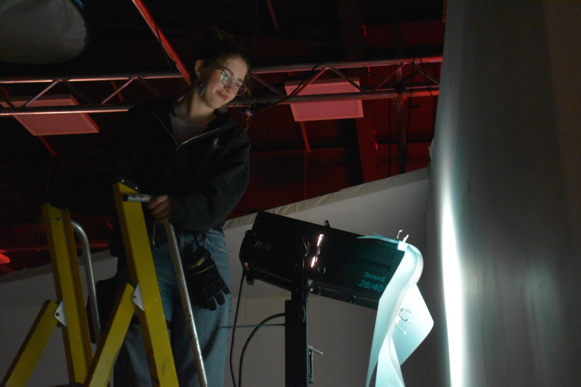 BA (Hons) Film Production student B Matthew at the top of a ladder next to a film light, on set at Elliott Road studios.