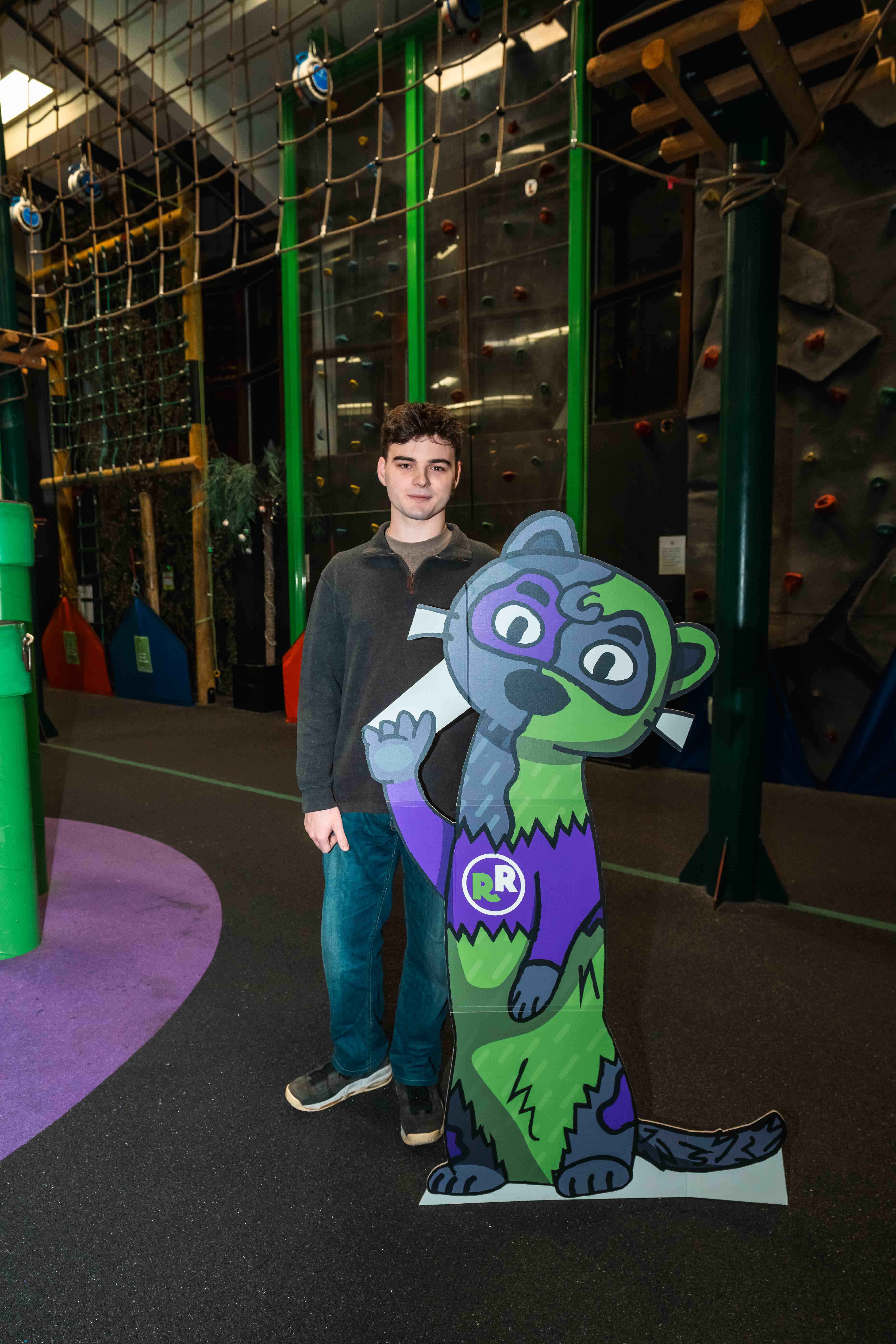 BA (Hons) Graphic Design student B Roberts standing next to a cutout of a green and purple otter mascot at RockReef on Bournemouth Pier.