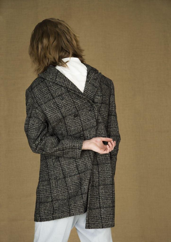 Image of a person facing away from the camera, wearing a coat back-to-front, with one arm behind their back.
