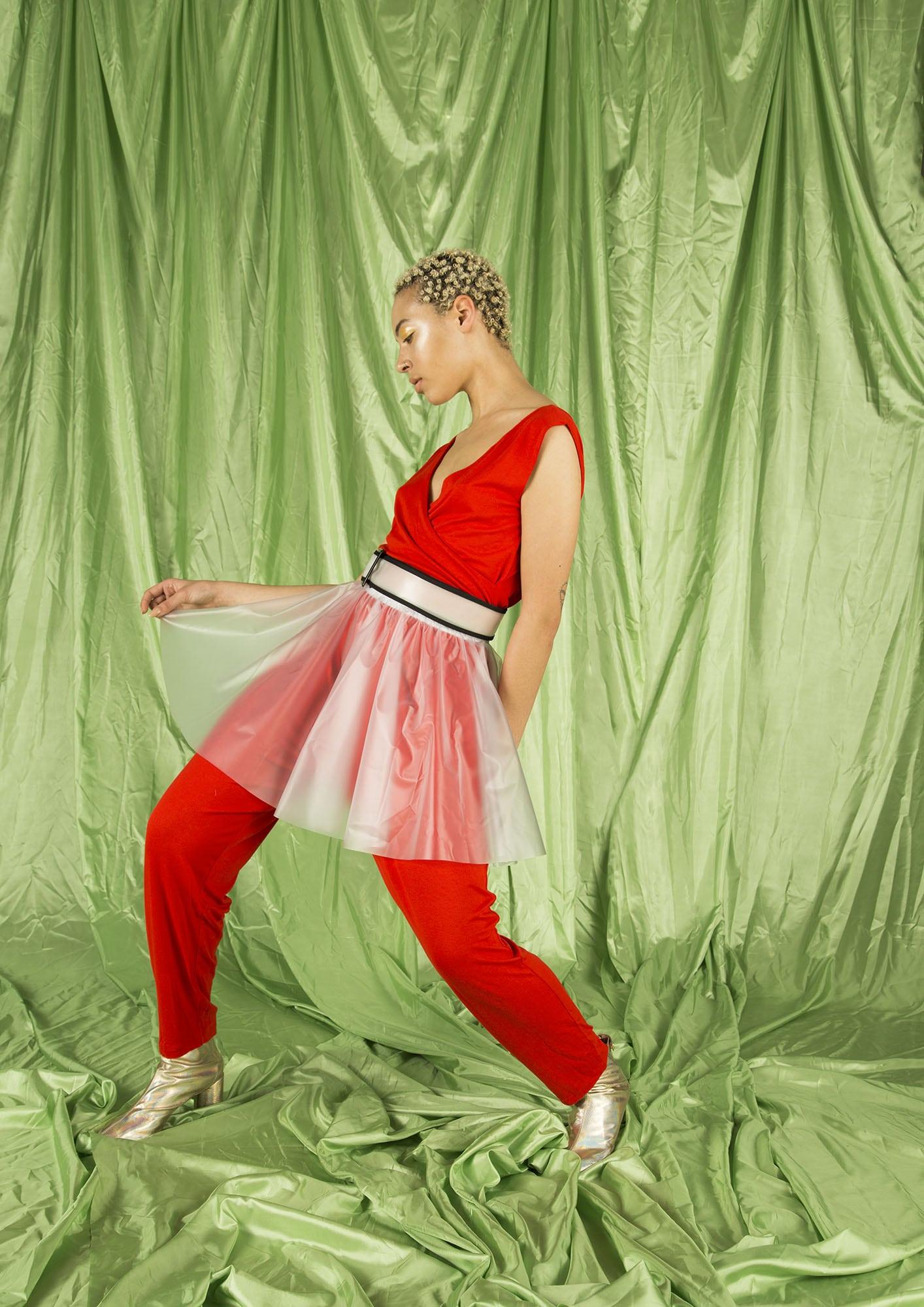 Lady in a red outfit with a transparent skirt poses for a photo on some loose-hanging backdrop curtains.