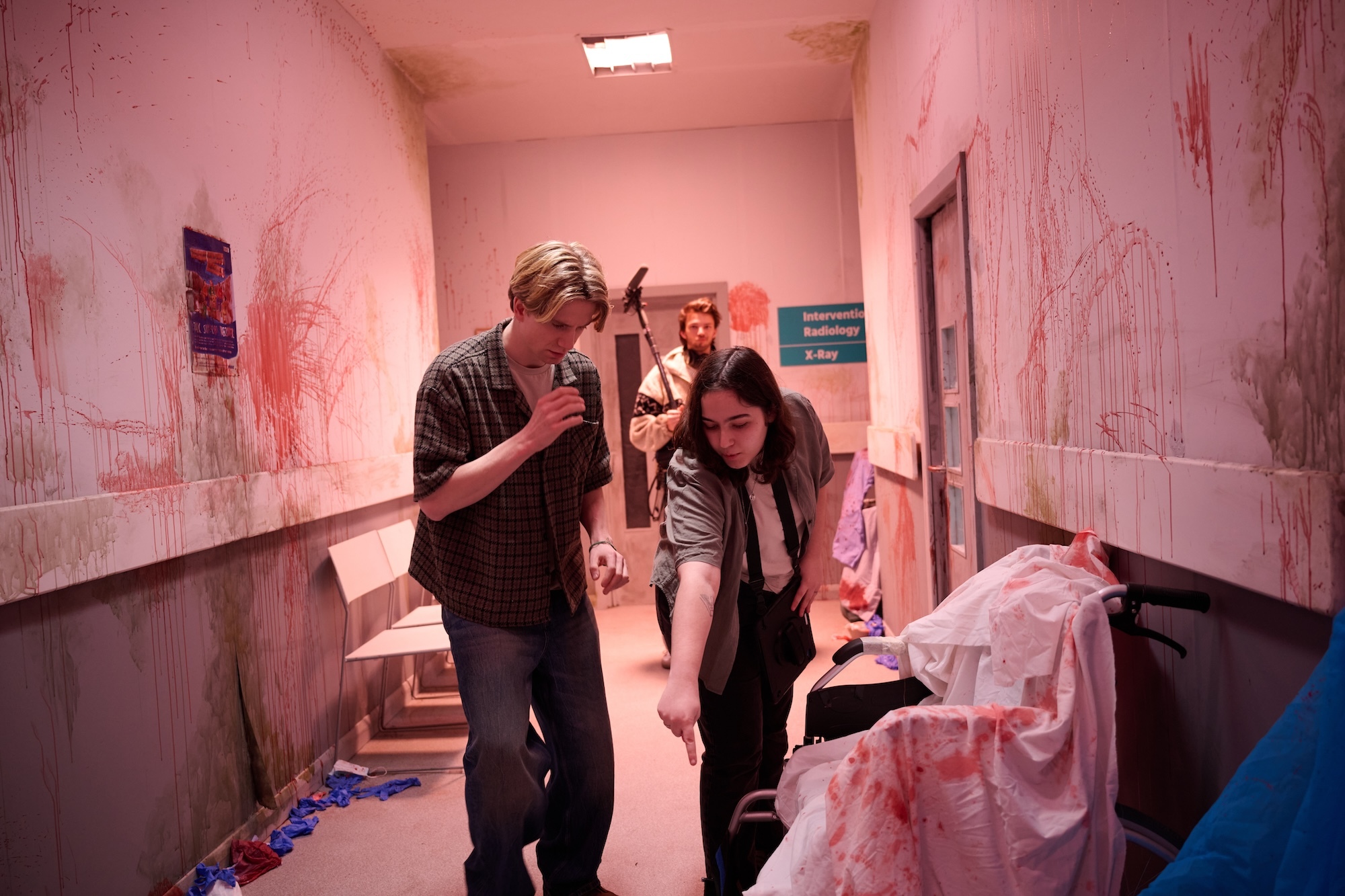 BA (Hons) Film Production student B Barr directs an actor, pointing down towards the floor in a hospital corridor with bloodstained walls. A boom mic operator is visible in the background.