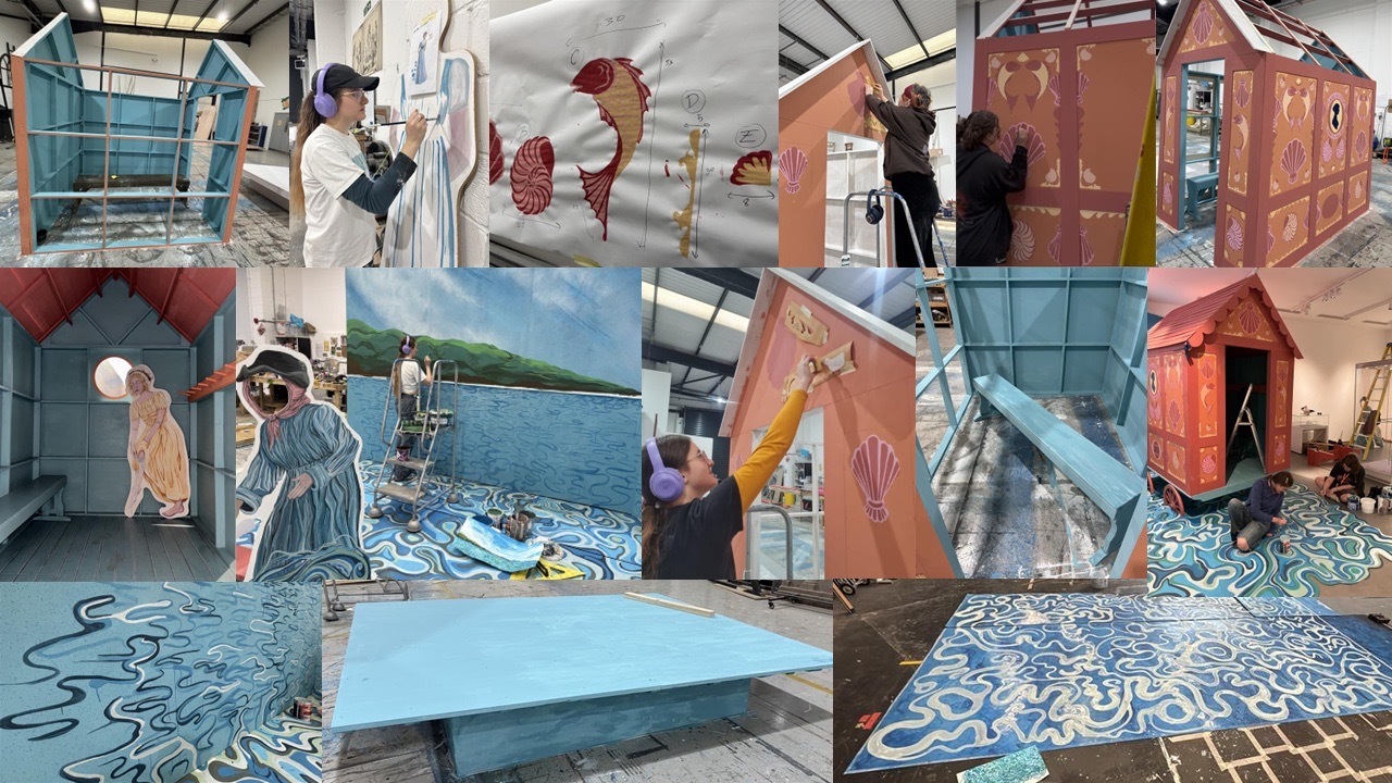 Artist's studio with large geometric sculptures in orange, red, and blue. Paint buckets, canvases, and decorative floor patterns visible.