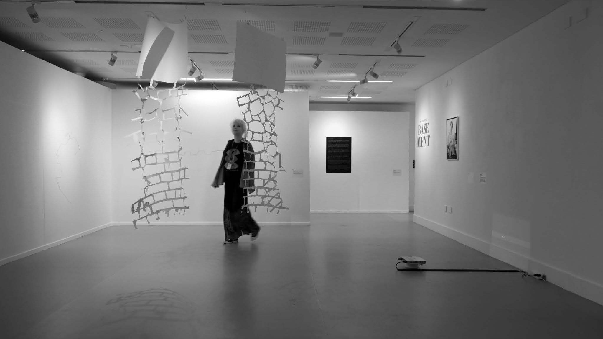 Person walking through an exhibition space by Bhavanda's work, black and white.