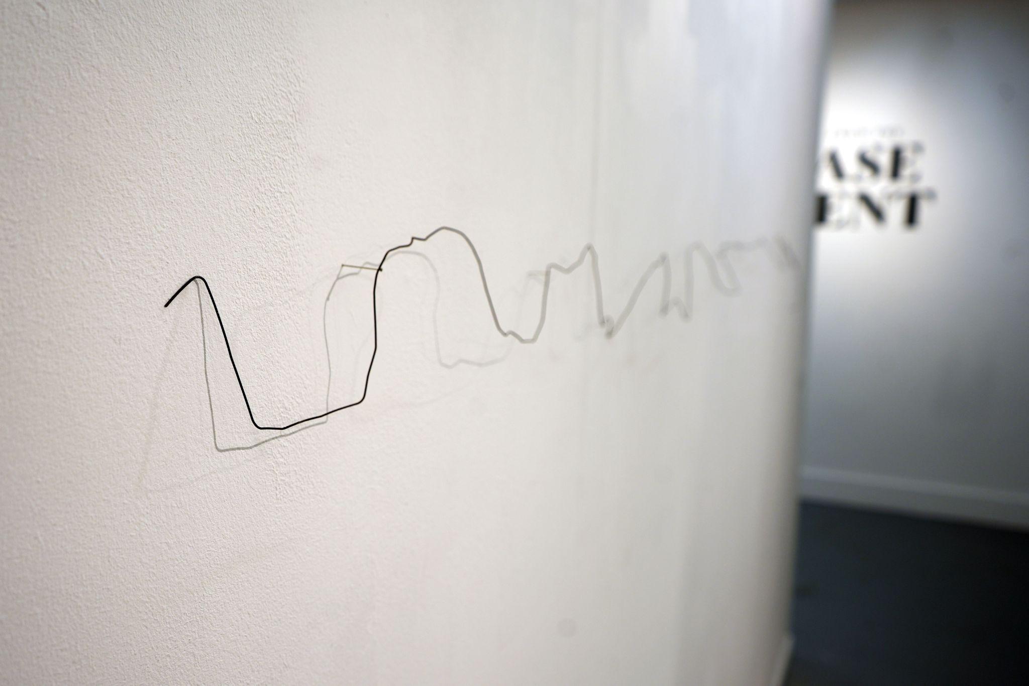 A piece of wire trailing along a white wall, moulded to the shape of bricks.