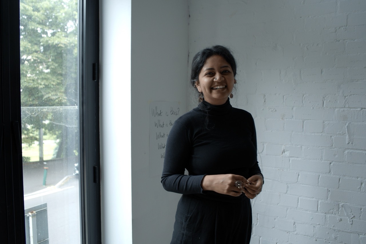 Bhavana Rao smiling in front of a white wall, wearing black.