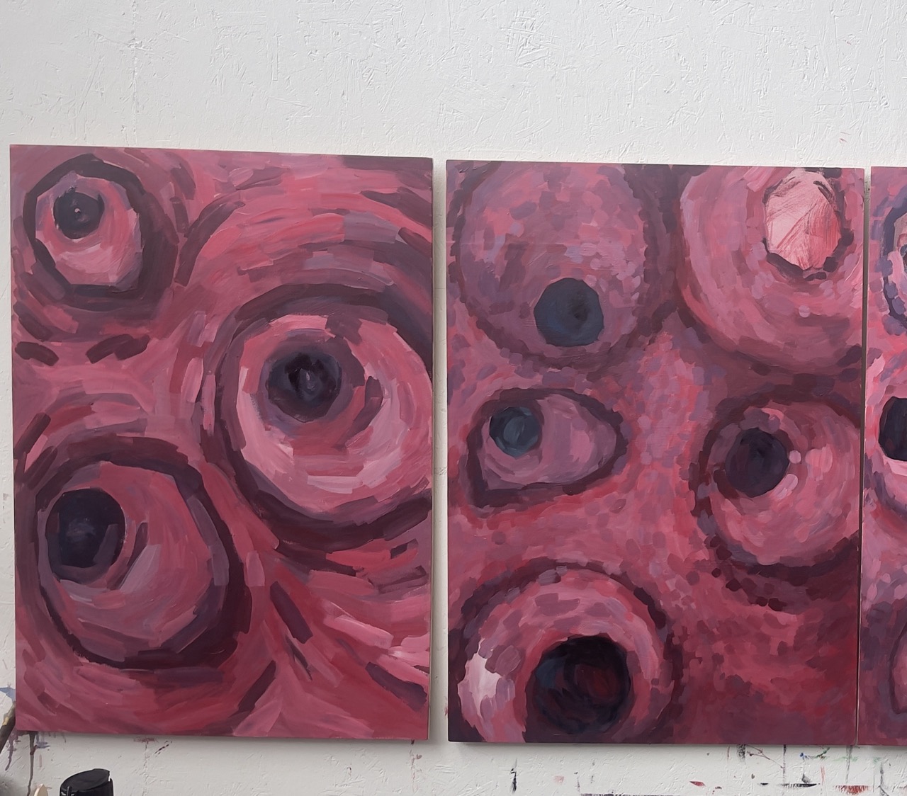 Two large abstract paintings dominated by shades of red and dark purple. The artworks feature circular shapes with varying sizes and depths, blending into the background while showcasing textured brush strokes.