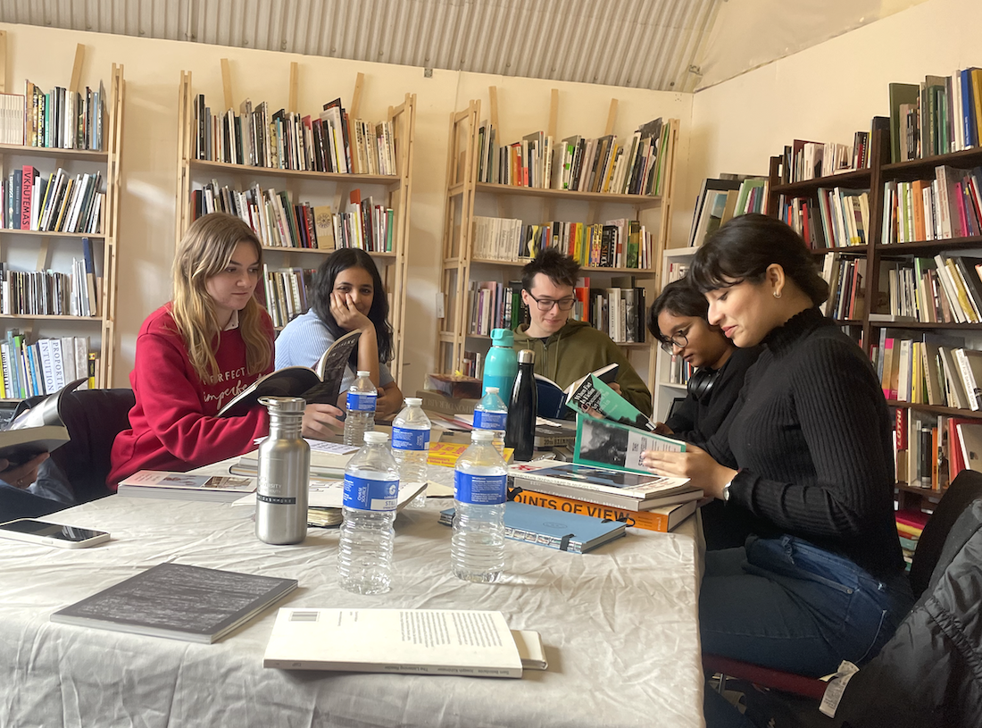 Five student sitting around a table and reading books in the Biblioteka library. Several bookshelves are standing in the background.