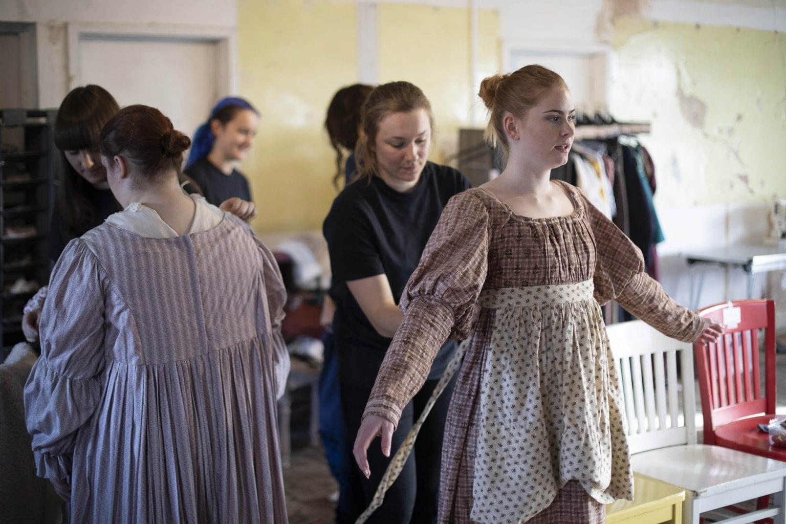People gathered in a backstage room in the middle of a costume fitting.