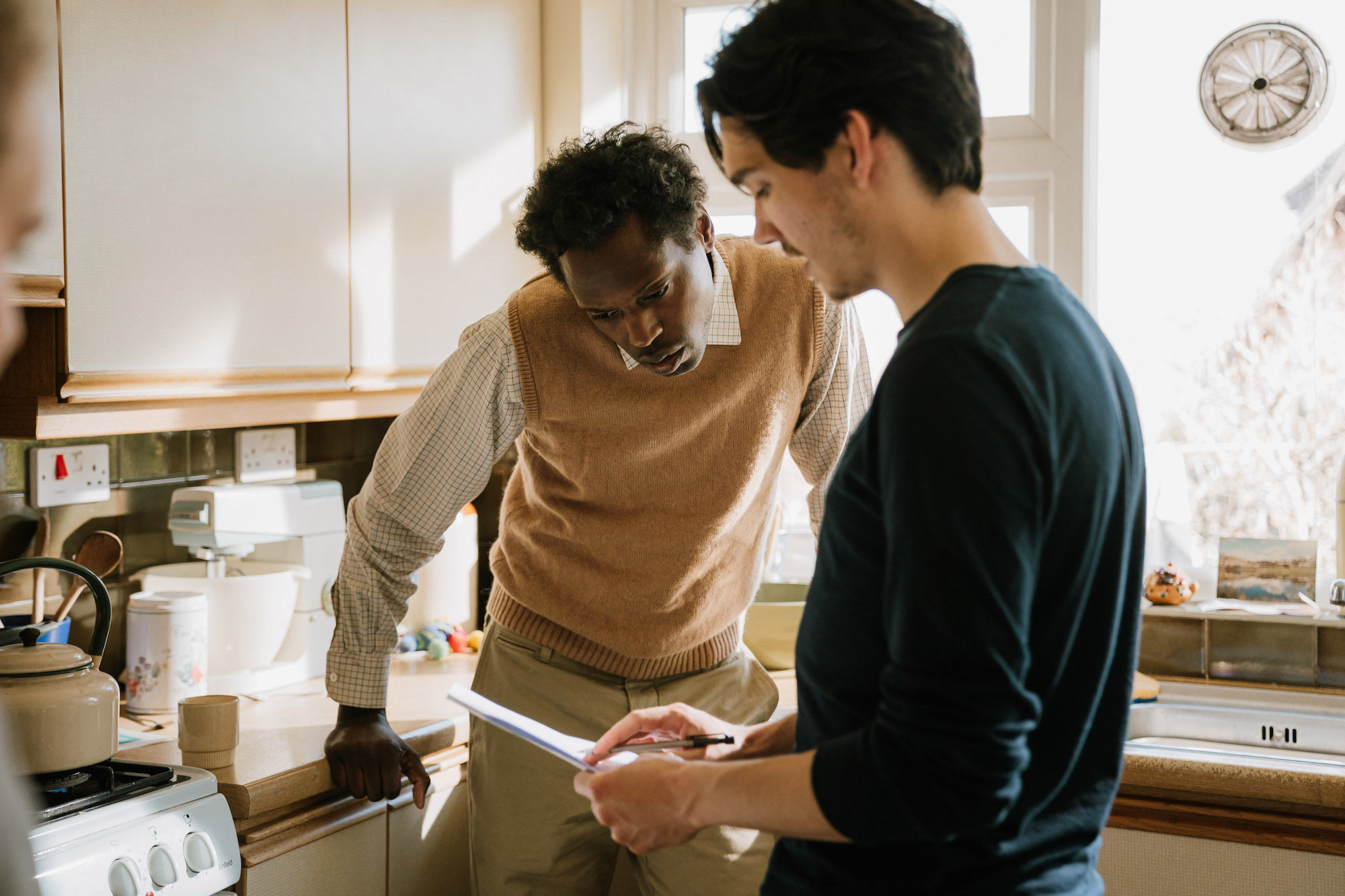 Two people stand in a kitchen in discussion over some paperwork.
