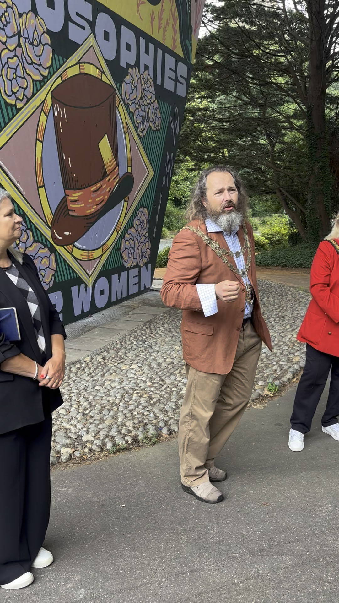 Cllr G Farquhar giving a speech outside a pillar of a flyover decorated with a mural in Bournemouth.