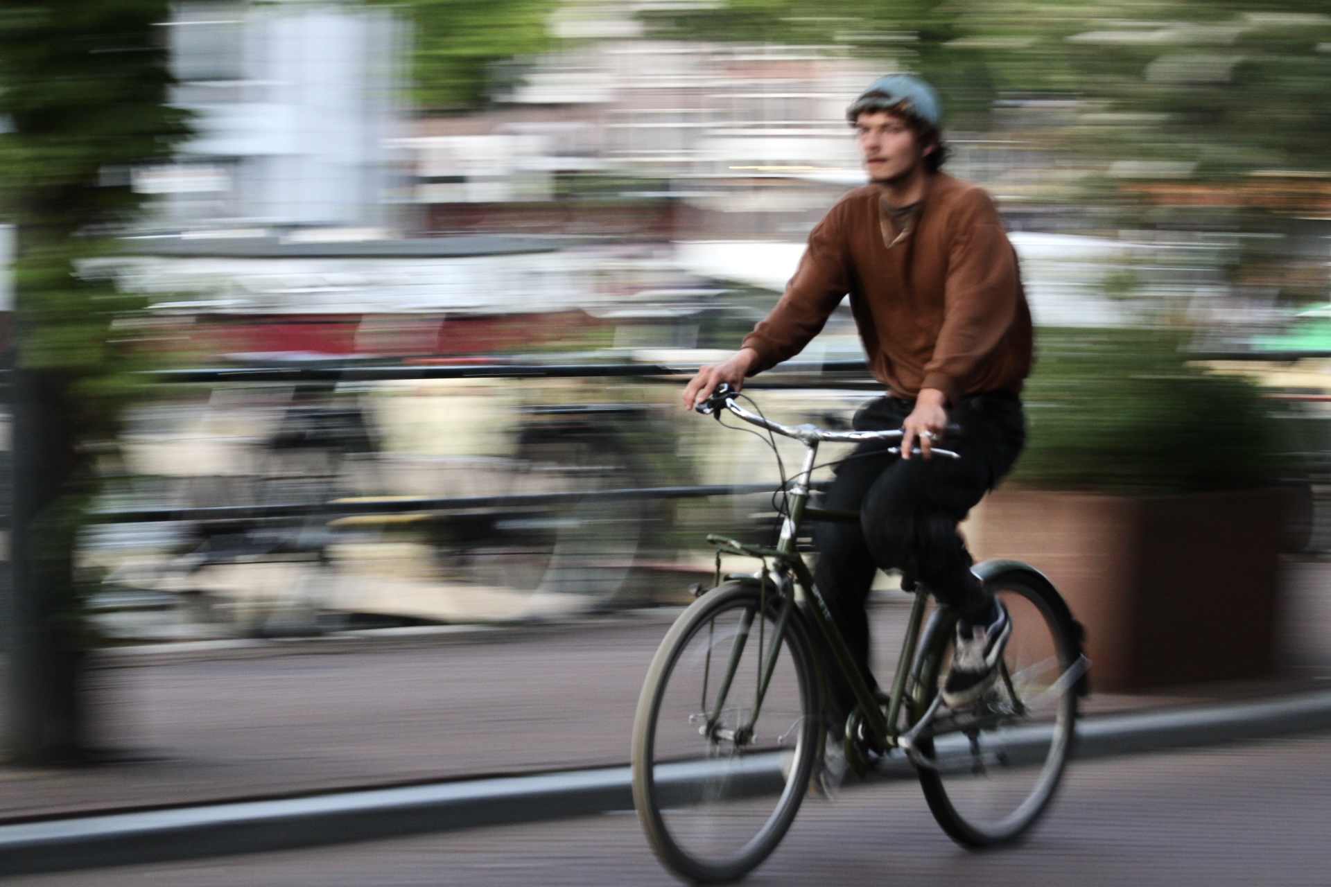 A person wearing a blue helmet rides a black bicycle on a city street, with motion blur and buildings in the background.