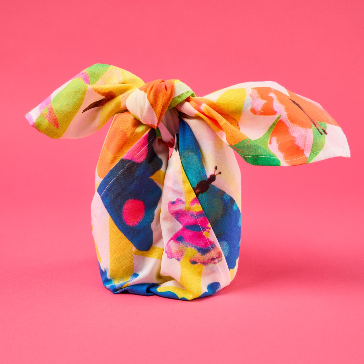 Multicoloured, pattered Lush Knot Wrap on a bright coral pink/red background.