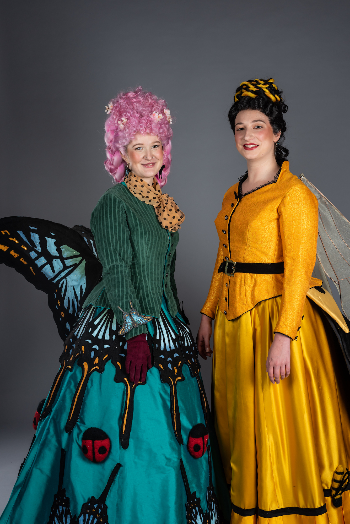 Two models wearing 19th century style gowns. The left dress is inspired by butterflies, the right dress is inspired by wasps.