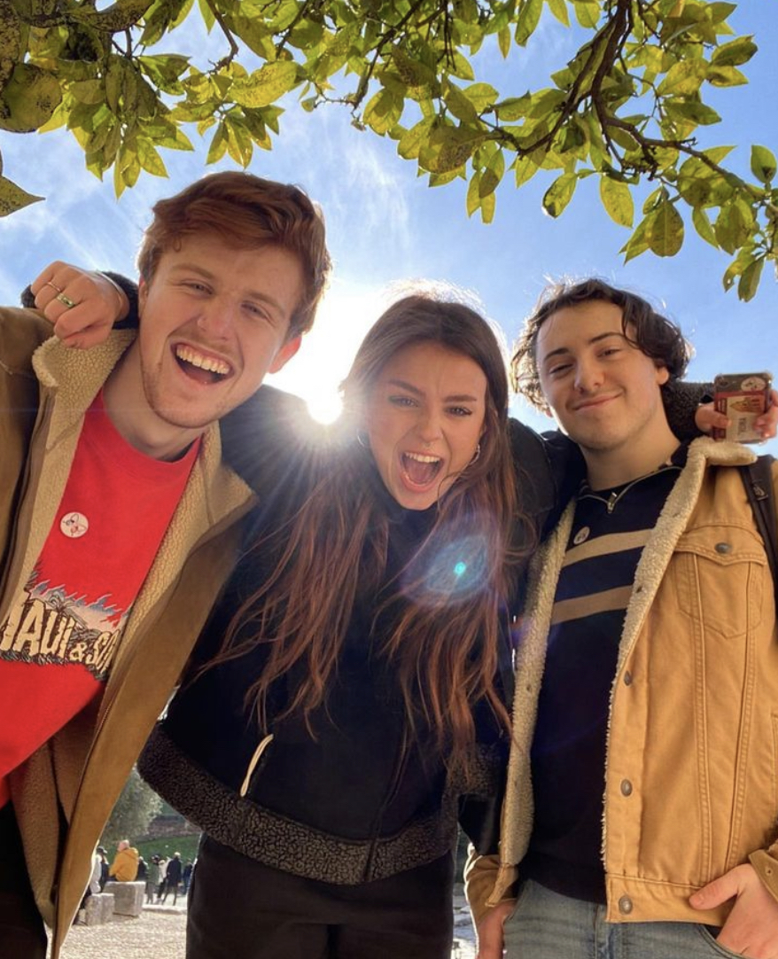 Three AUB students smiling and posing for a photo under a tree with the sun shining behind.
