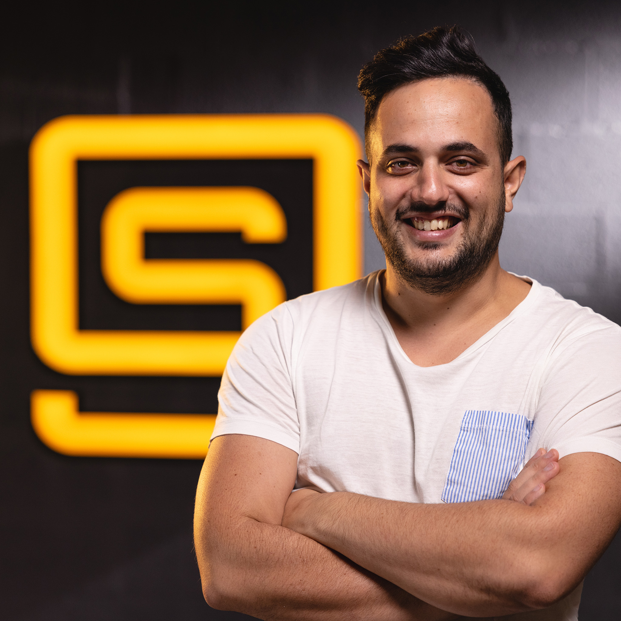 Headshot of A. Grima with an orange studio logo in the background.