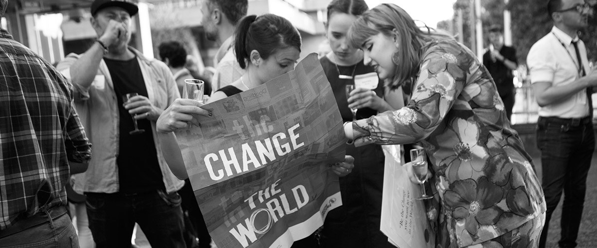 Three people in a crowd holding a poster with the text 'Change the world'.