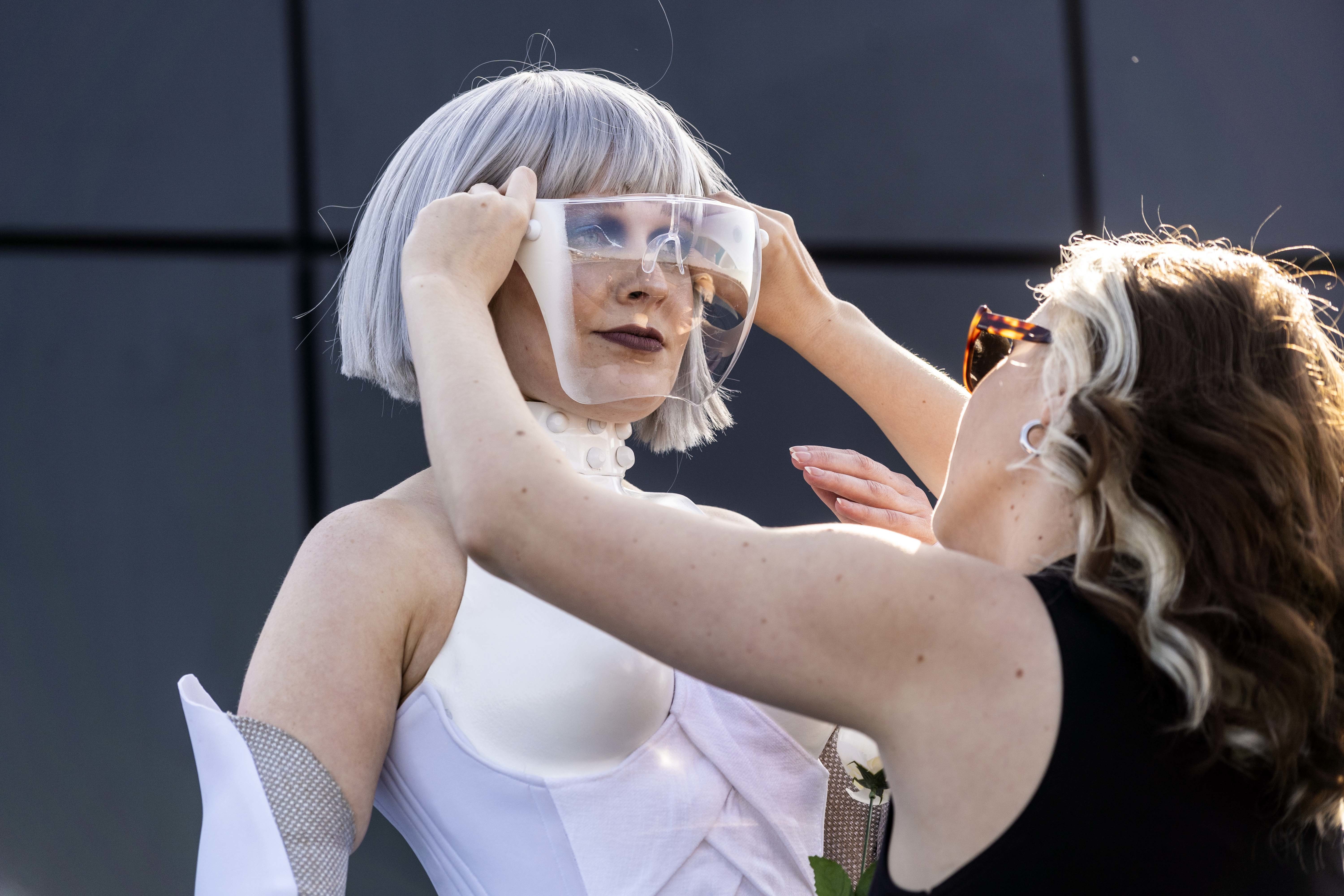 A person adjusts a mask on the face of a model who is dressed in a Hunger Games-inspired costume.