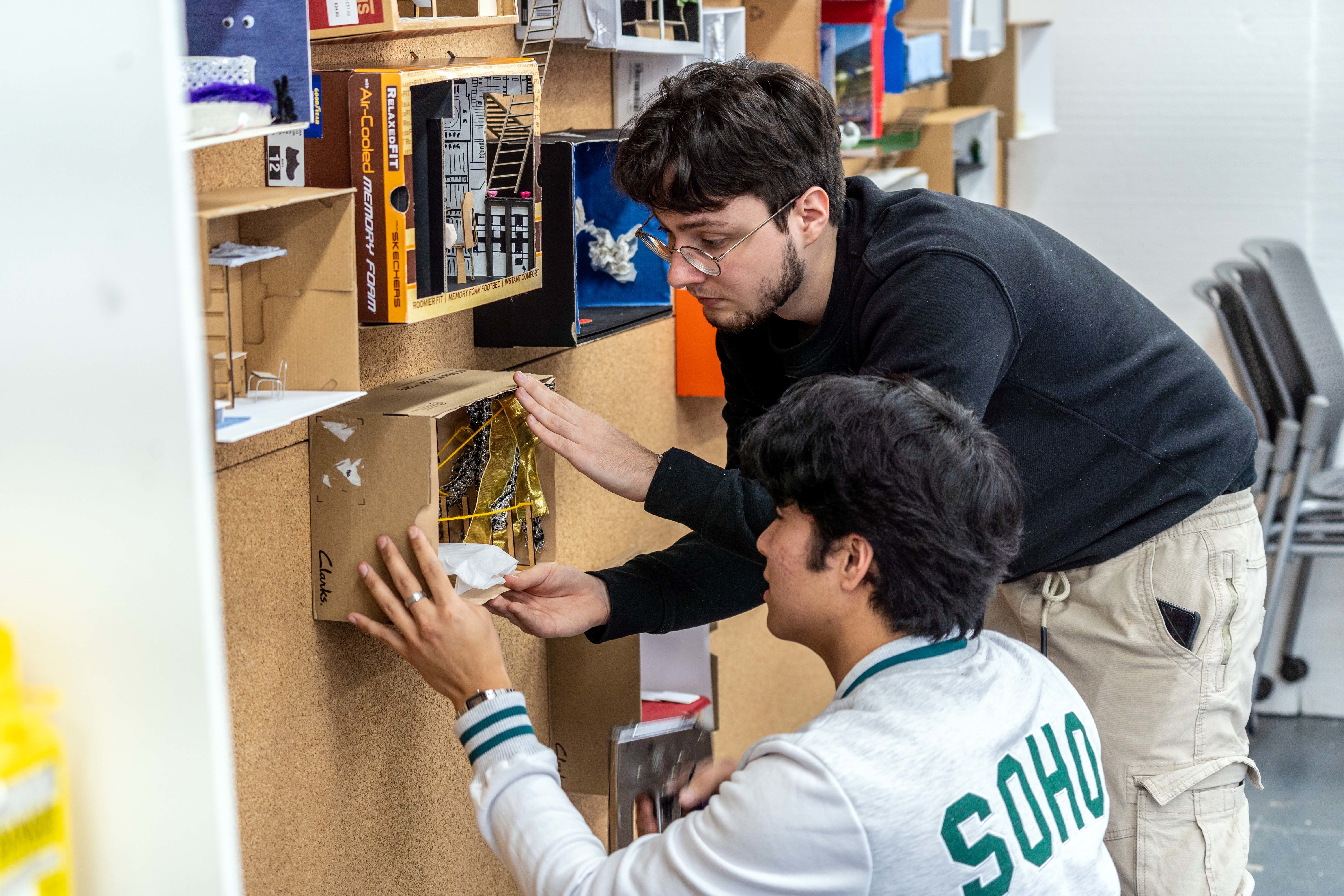 One person kneeling and another leaning over by a display board. Both are holding a box in place on the board.