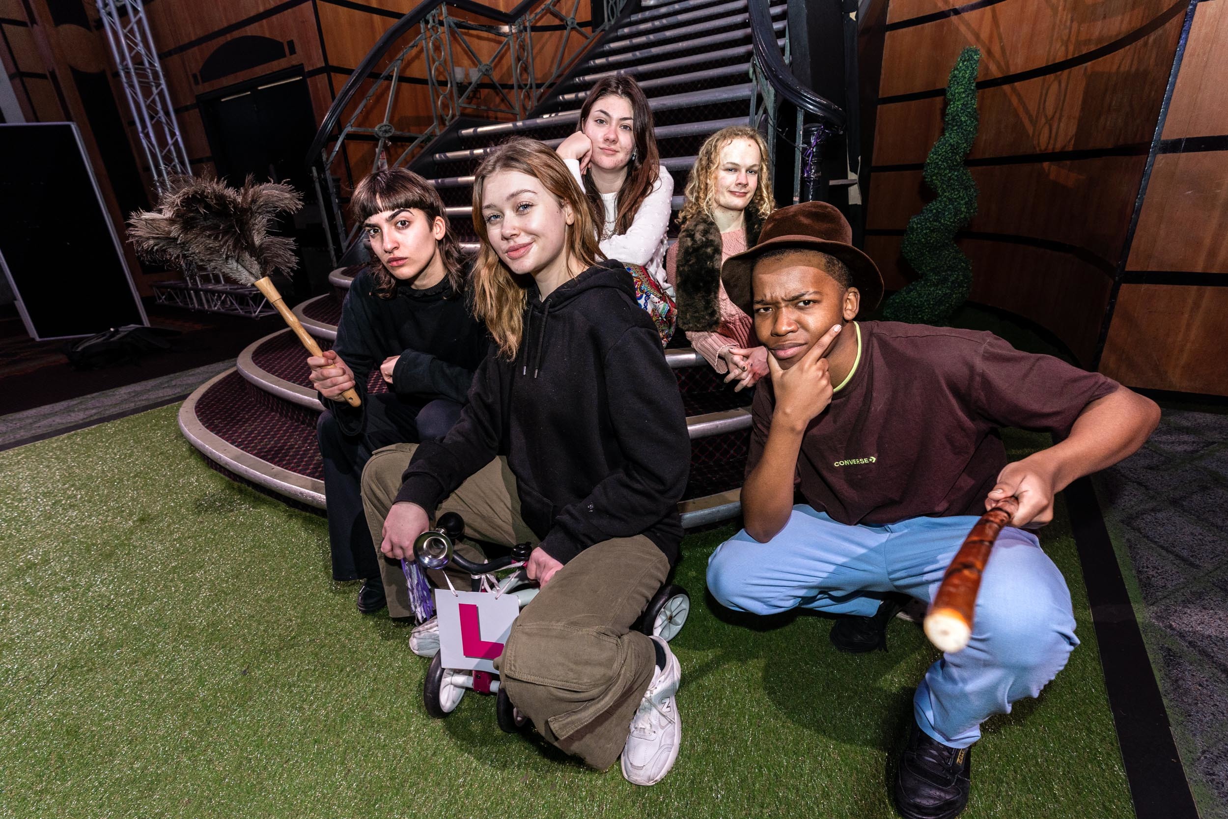 Five people sit at the foot of a staircase on a stage and pose for a photo.
