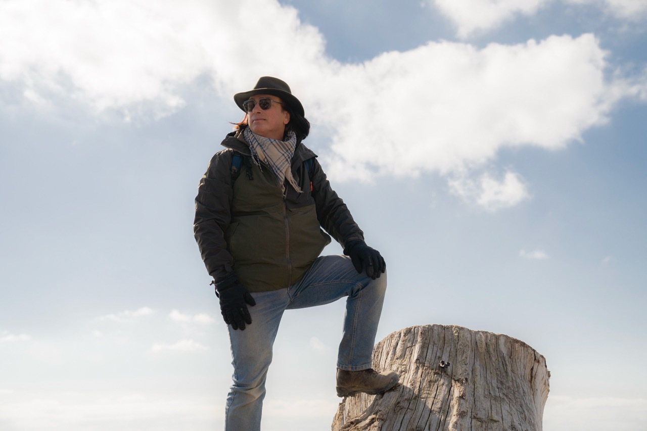 Kevan Manwaring stood on a cut tree, clouds and sky in the background.