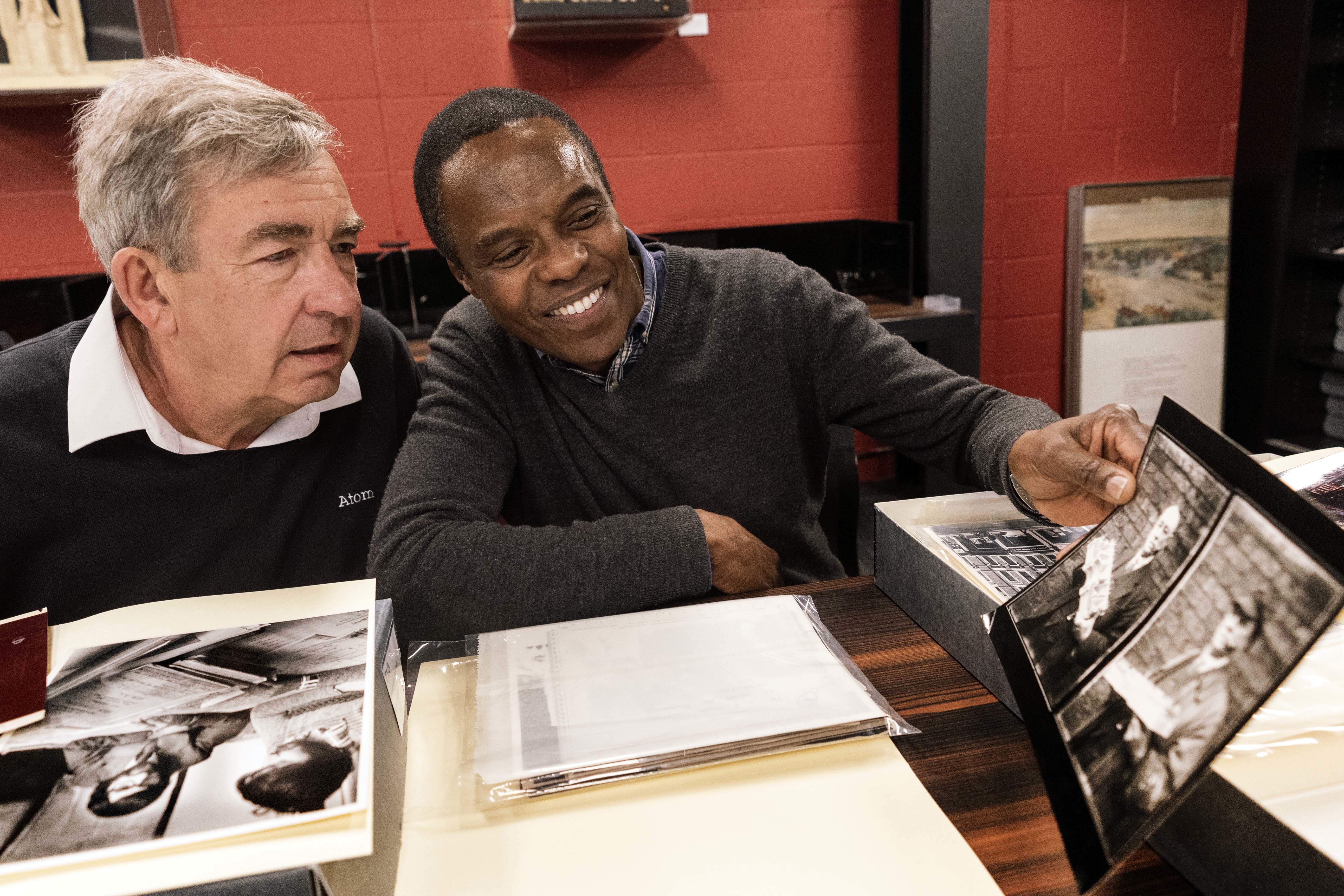 Two people sitting at a desk looking at a photo. Other documents are on the desk in front of them.