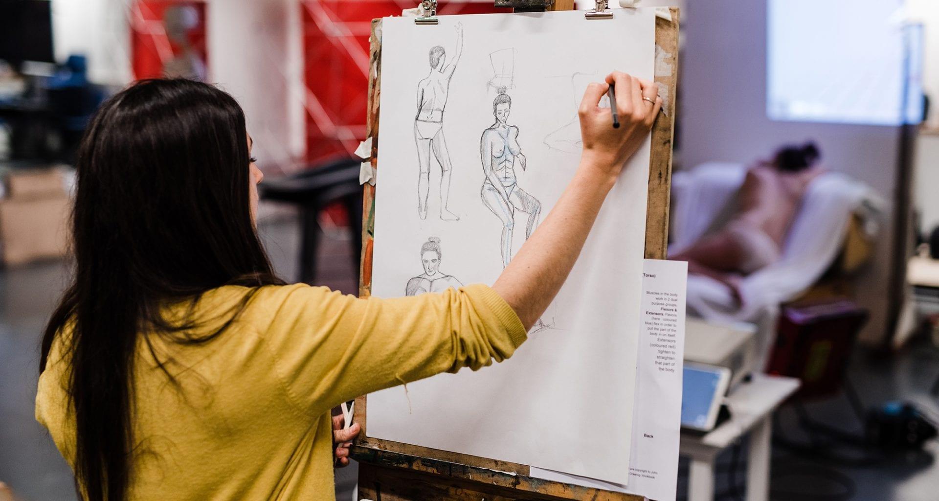 An artist standing by an easel with a piece of paper on it and drawing.