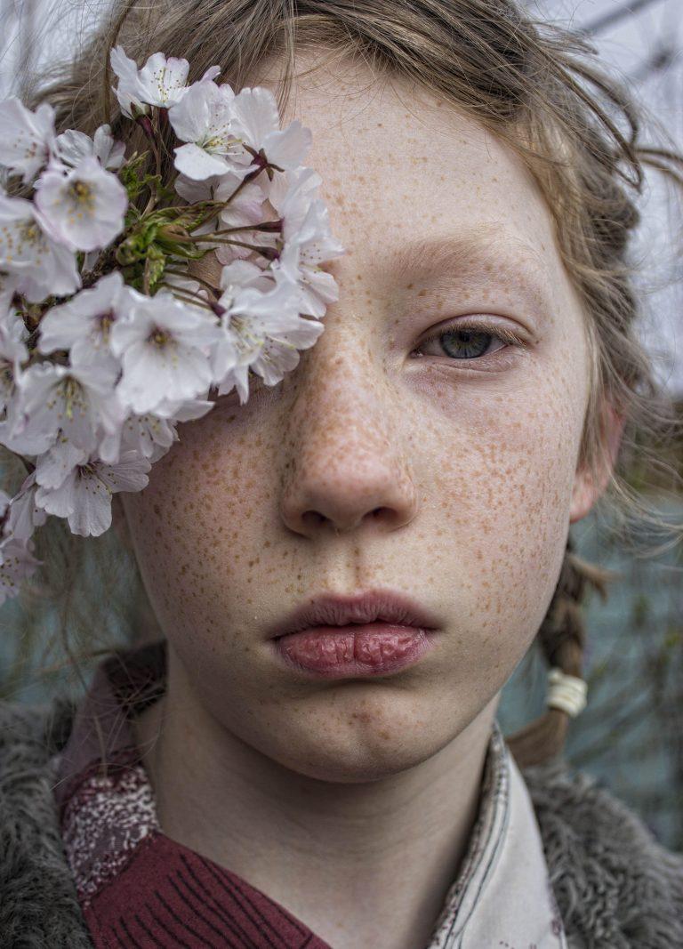 Headshot of a child with a bunch of flowers covering their right eye.