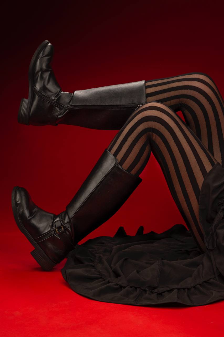 Close-up of a pair of legs wearing striped tights and black leather boots, on a red background.
