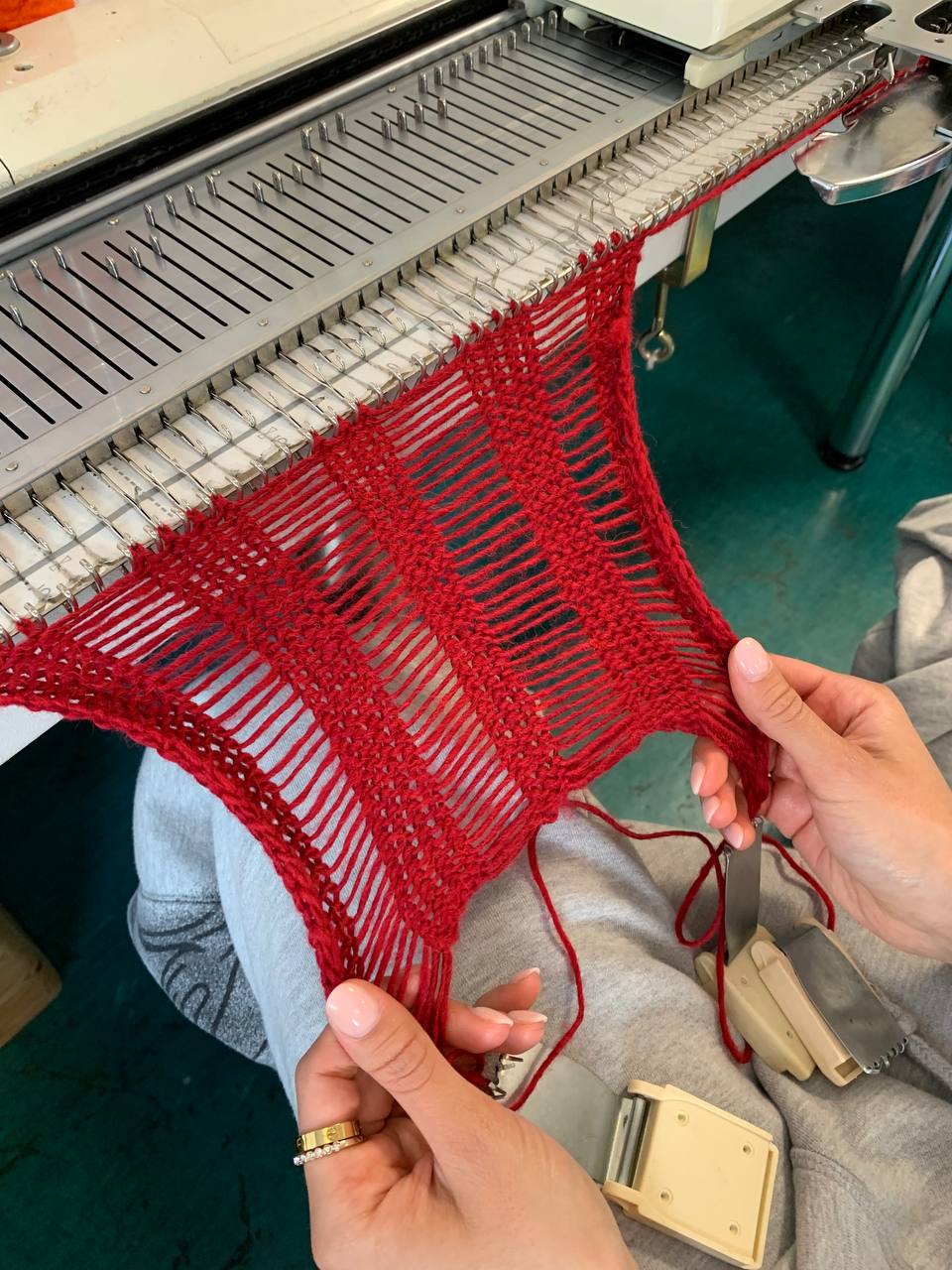 A person stretches a piece of red knitwear while it's attached to a knitting machine.
