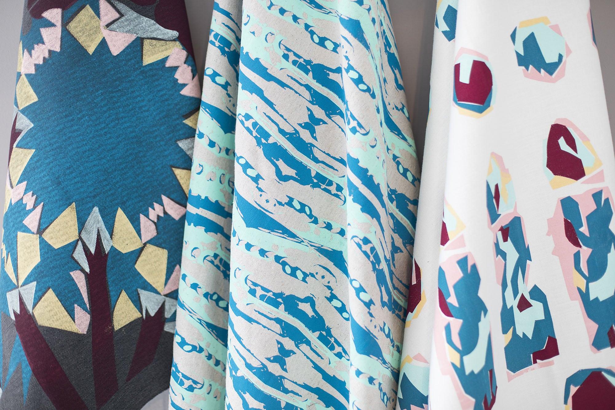 Three samples of different patterned fabric hanging in a gallery space.