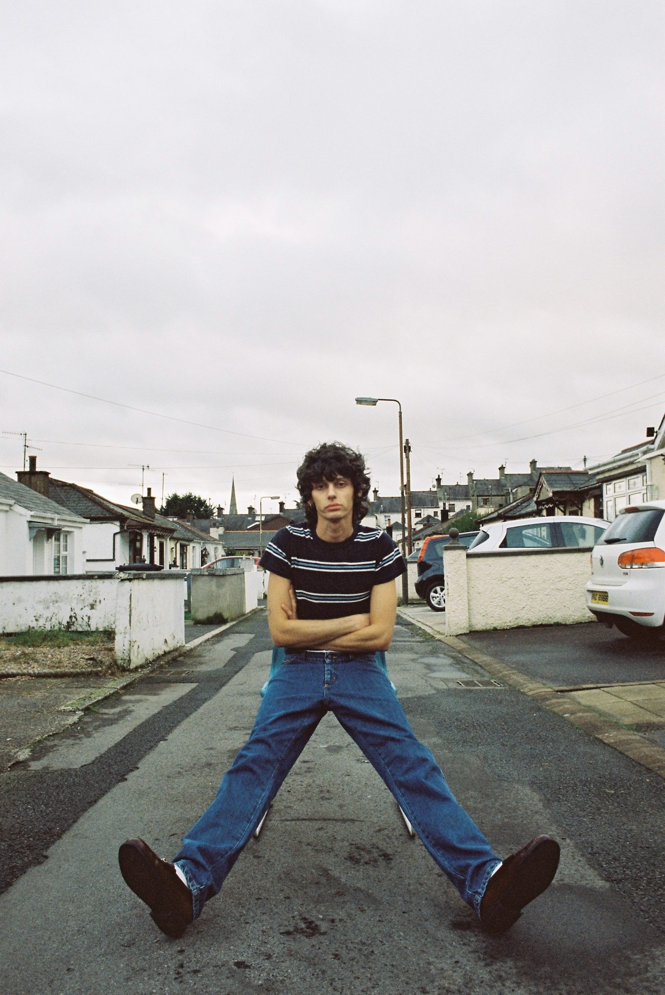 C McCabe sitting on wet street with legs spread wide, residential houses and cars in background